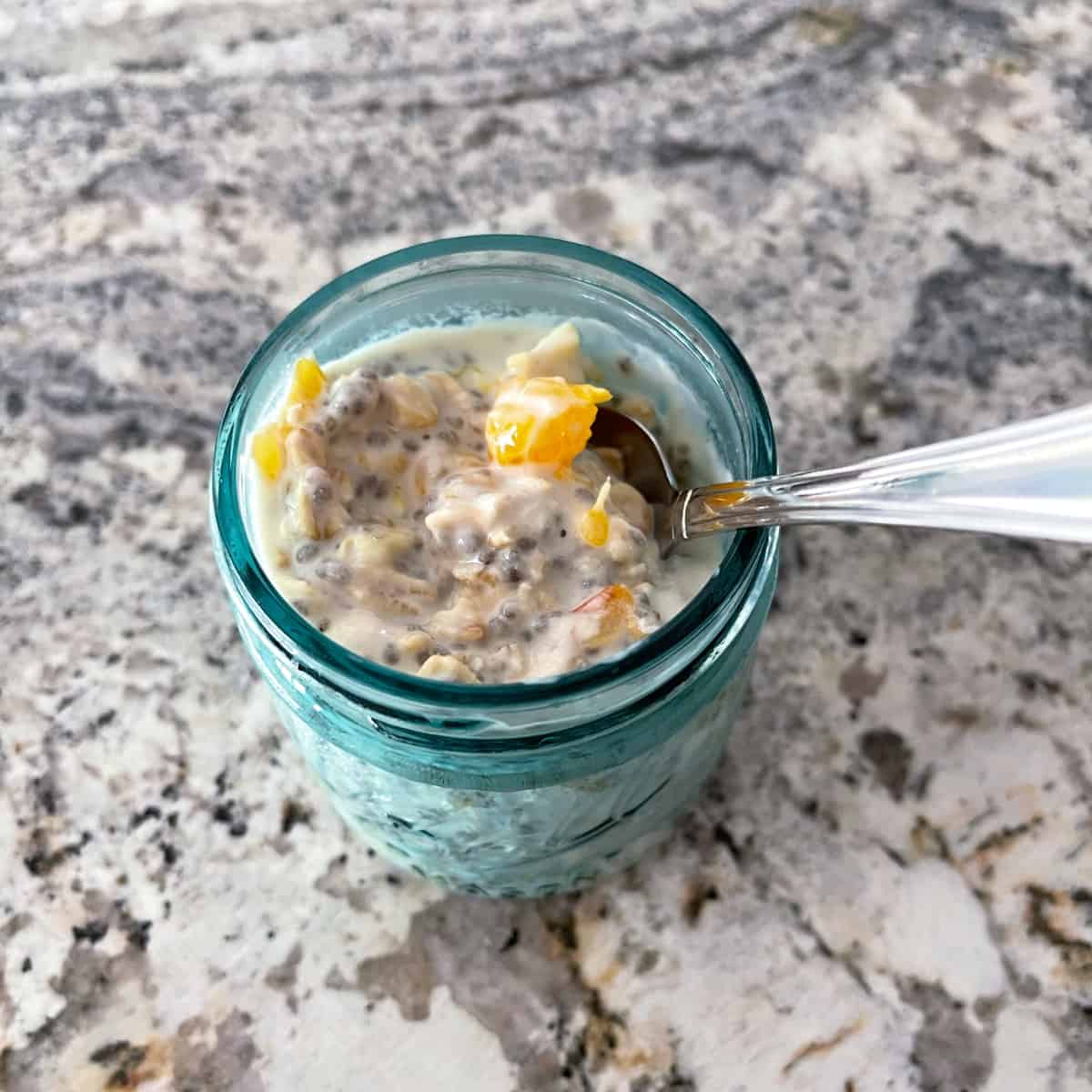 Overnight chia orange oats in small uncovered mason jar with spoon on granite.
