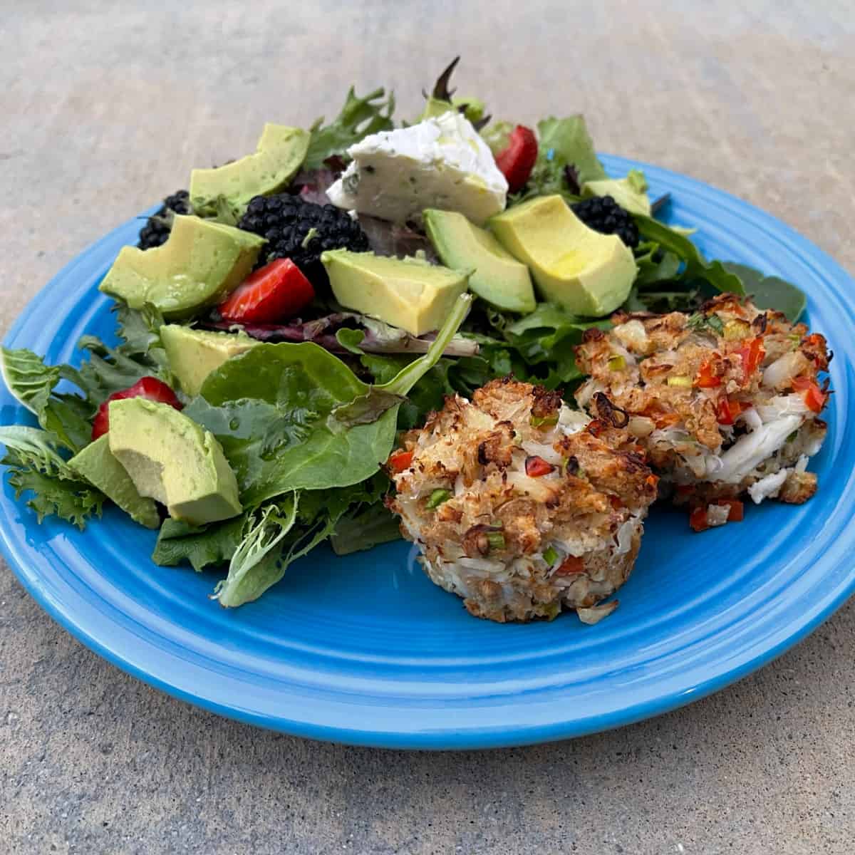 Muffin tin crab cakes with mixed green salad on blue plate.