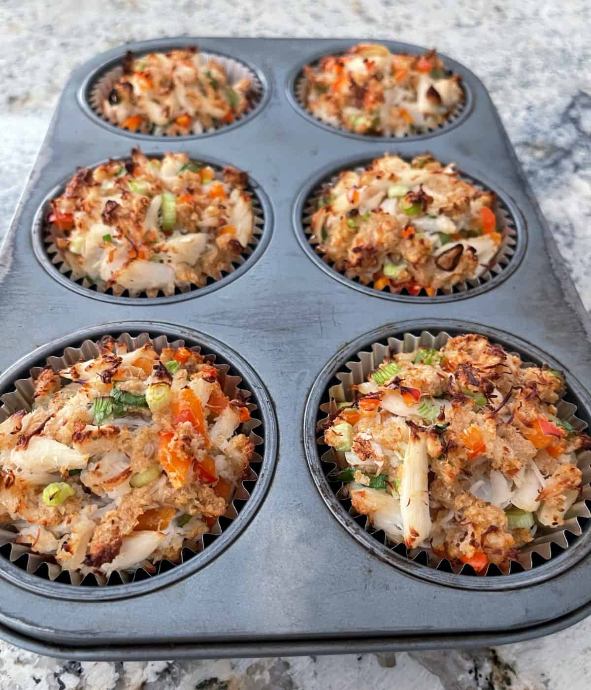 Six fresh baked crab cakes in muffin pan.
