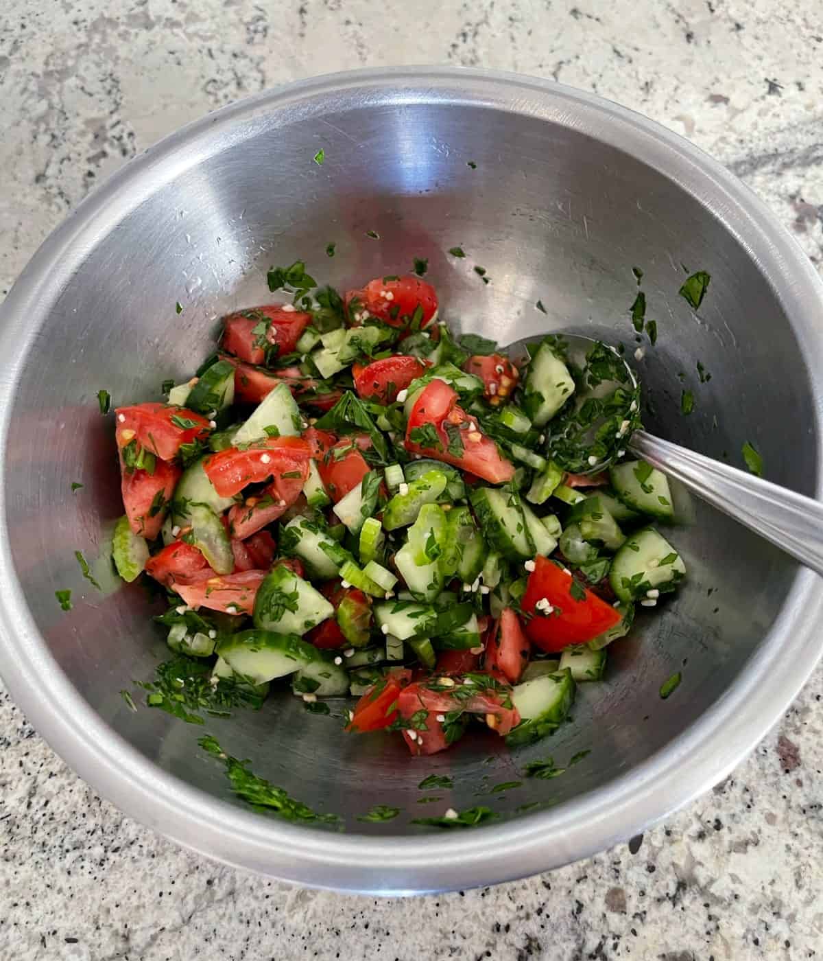 Stirring together chopped tomato, cucumber, celery, parsley, minced garlic and rice wine vinegar in medium bowl with spoon.
