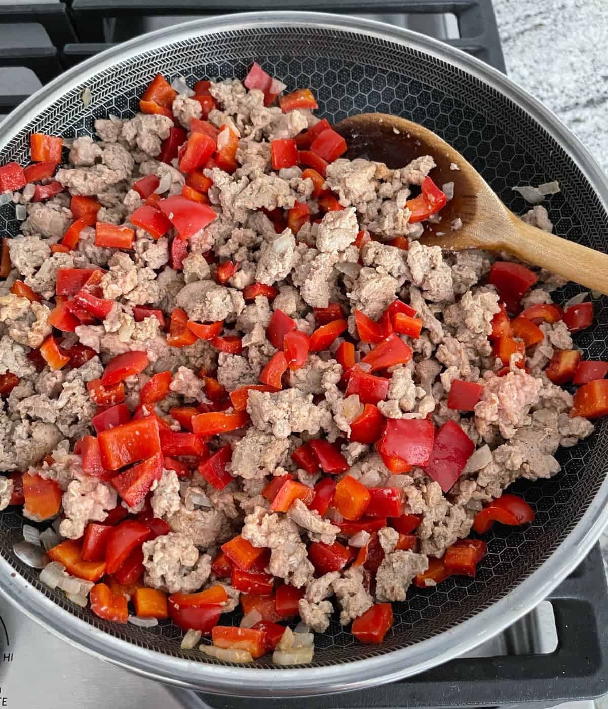 Cooking ground turkey, chopped red bell pepper and onion in skillet while stirring with a wooden spoon.