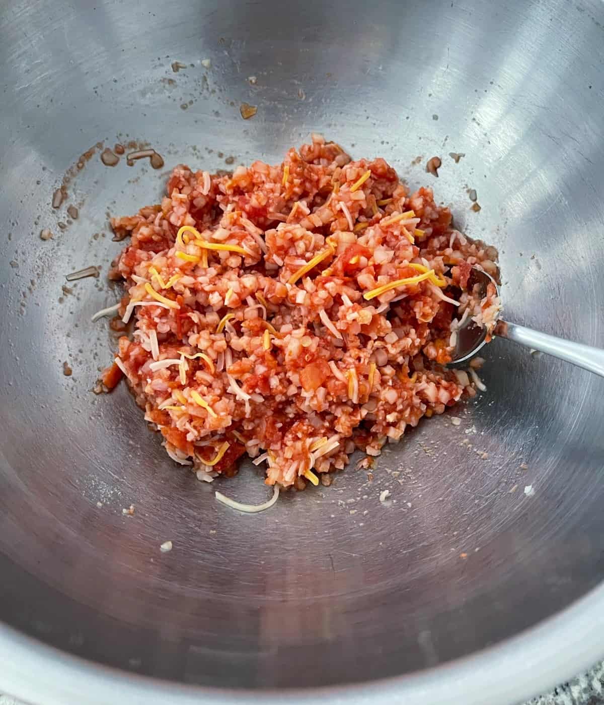 Stirring together cauliflower rice, crushed tomatoes, shredded cheese, garlic powder and onion powder in mixing bowl.