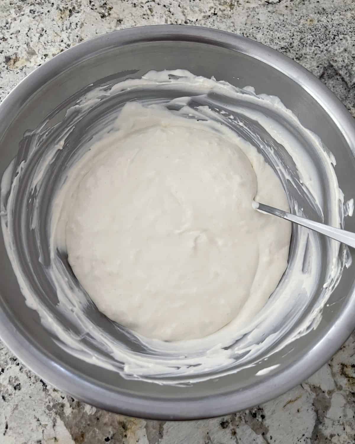 Stirring no-bake cheesecake dessert in mixing bowl with spoon.