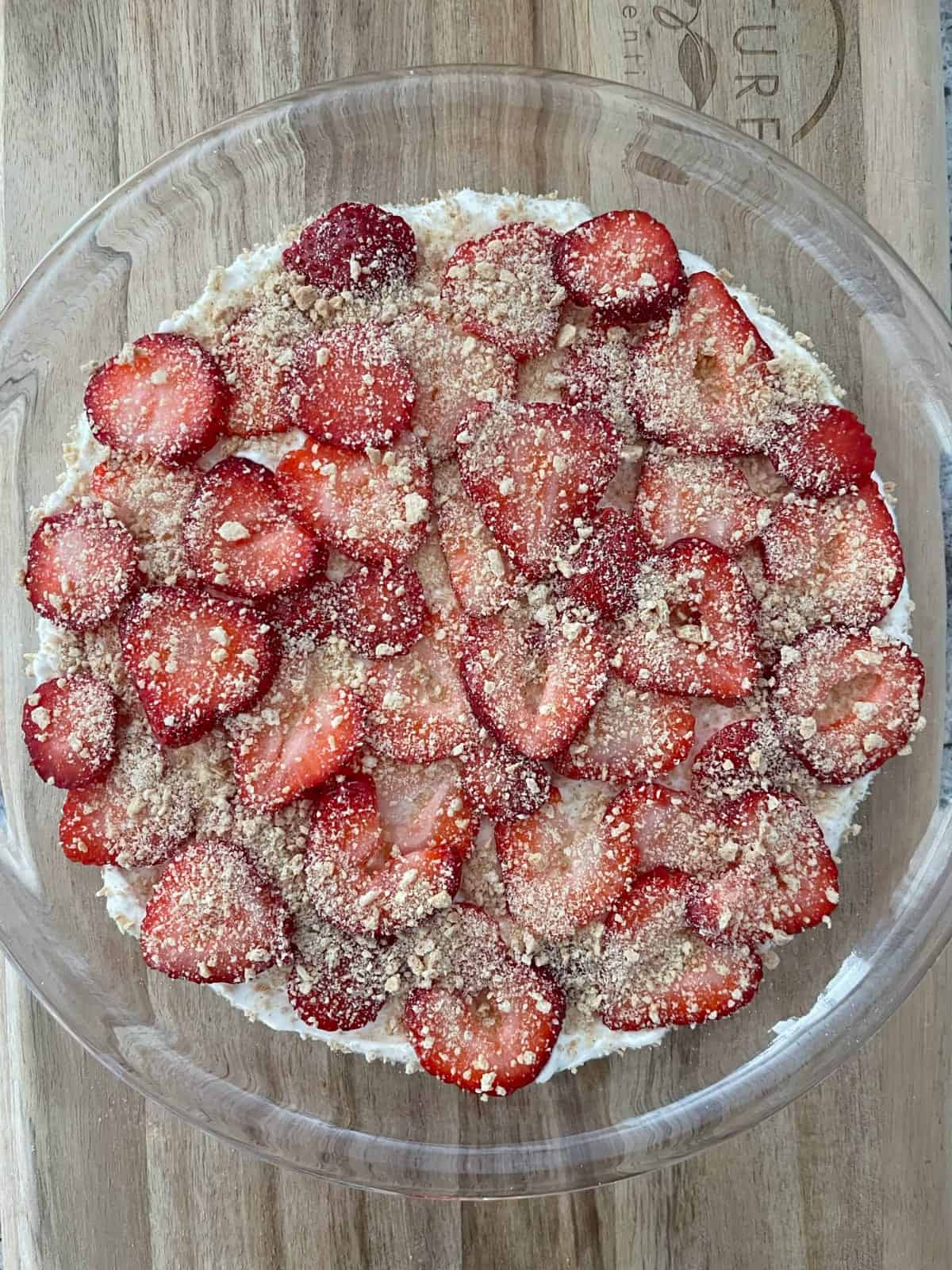 Scoopable strawberry cheesecake no-bake dessert in glass pie dish on wood cutting board.