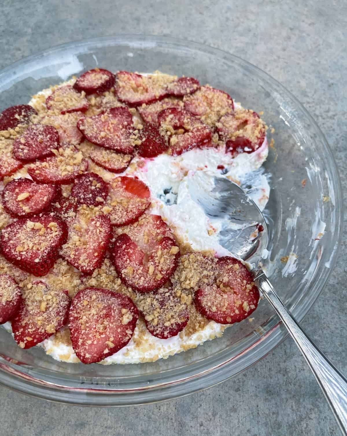 No-Bake Strawberry Cheesecake Dessert in glass pie dish with serving spoon.