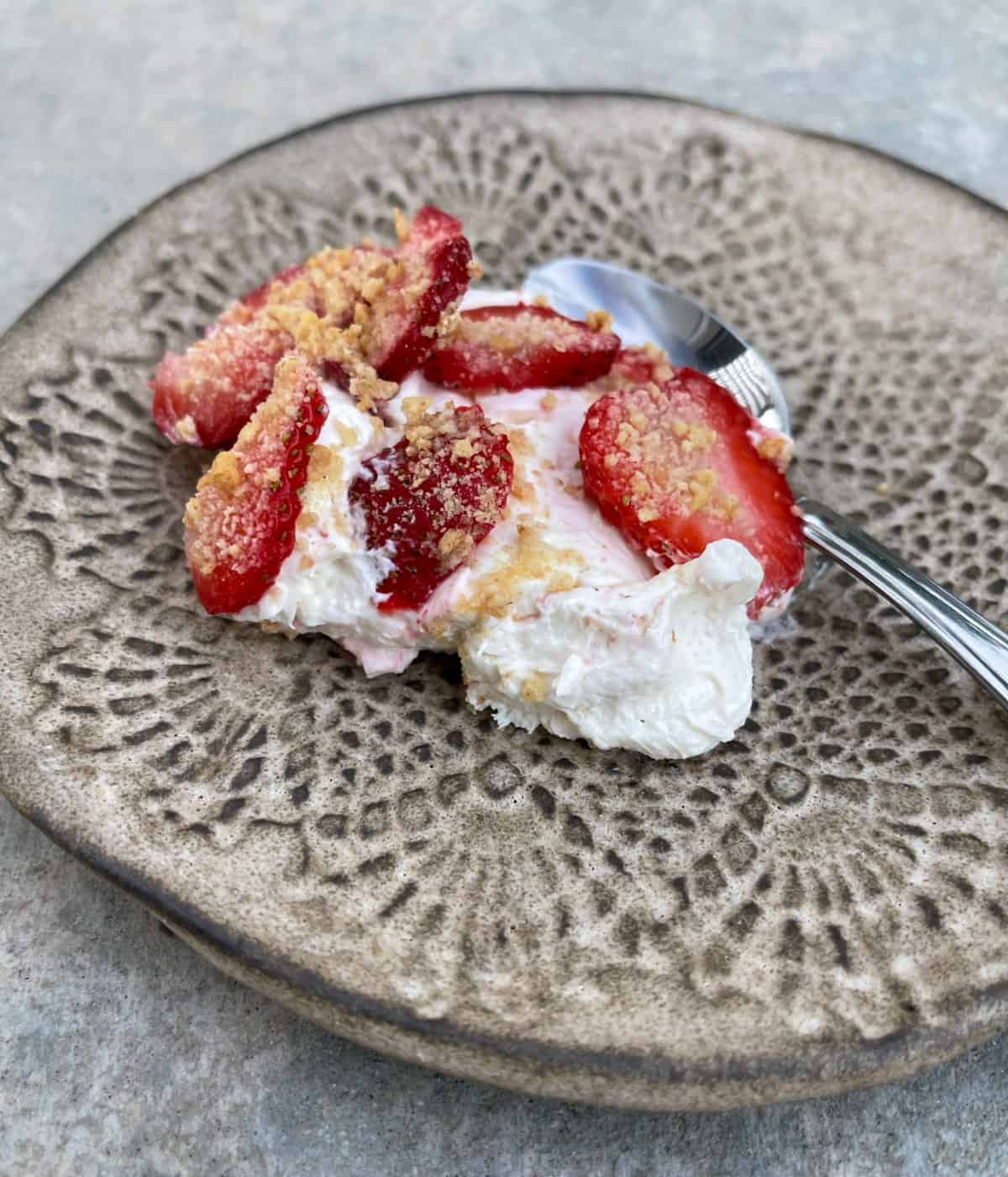 Single serving scoopable no-bake strawberry cheesecake on small plate with spoon.