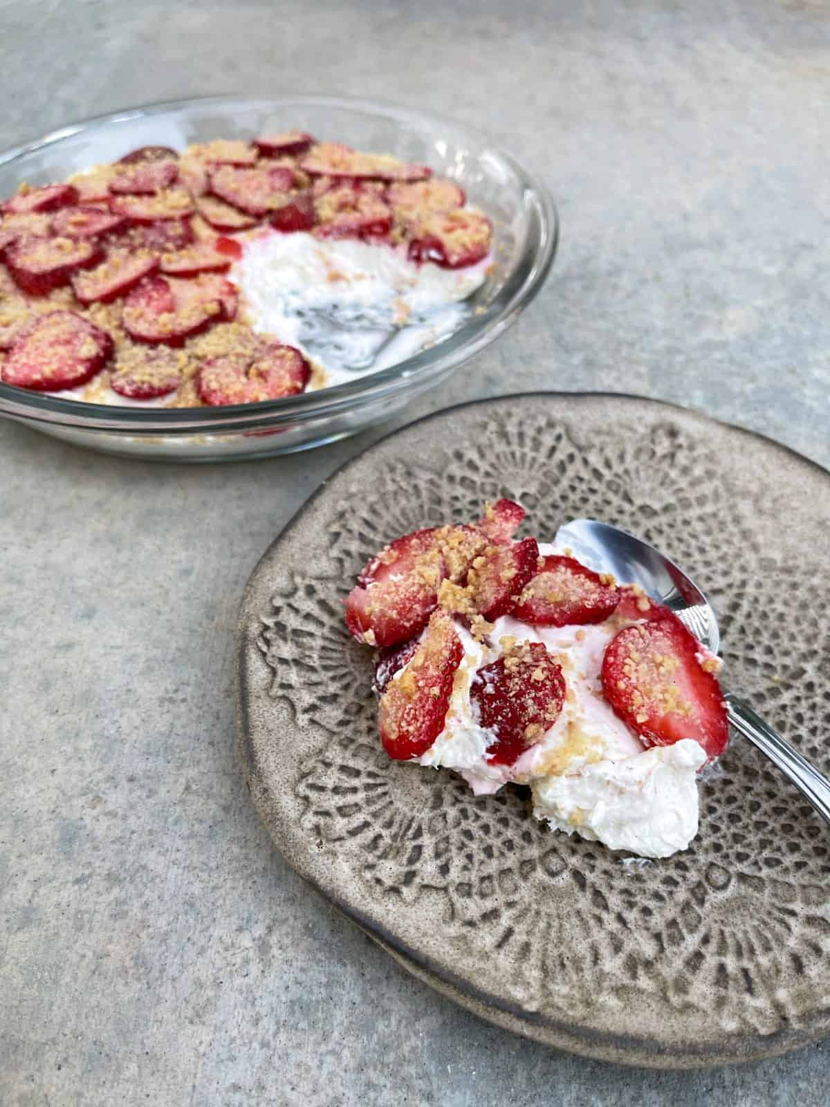 No-bake scoopable strawberry cheesecake dessert on small plate with spoon and whole pie dish in background.
