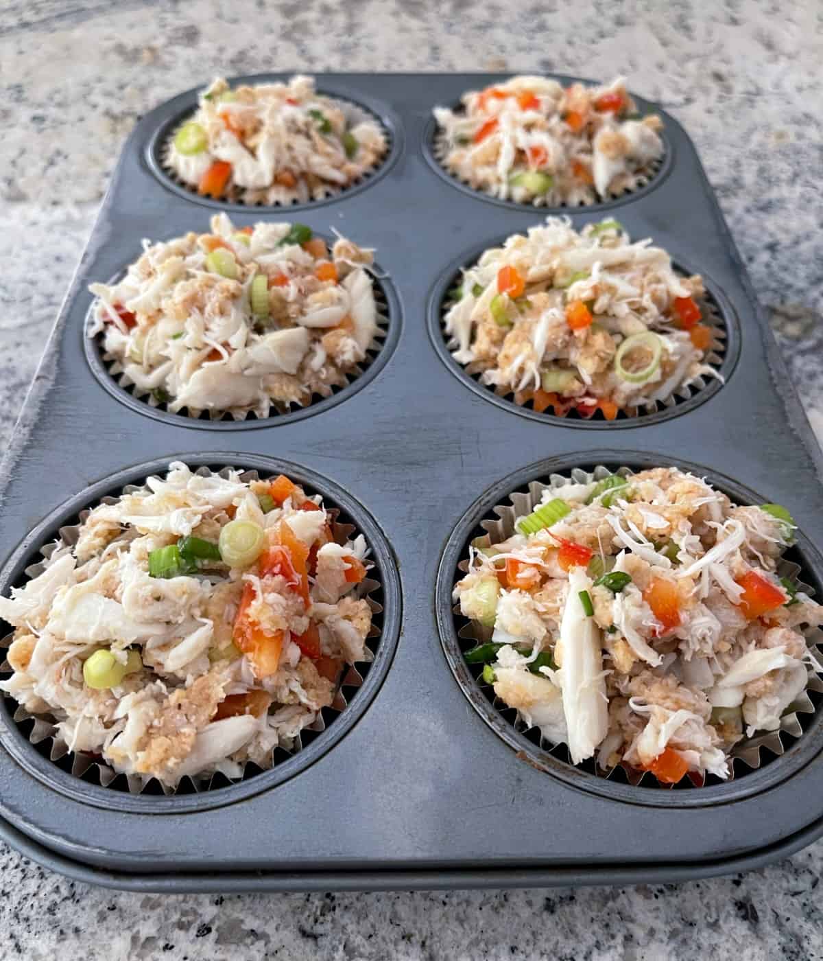 Unbaked crab cakes in foil-lined 6-cup muffin pan.