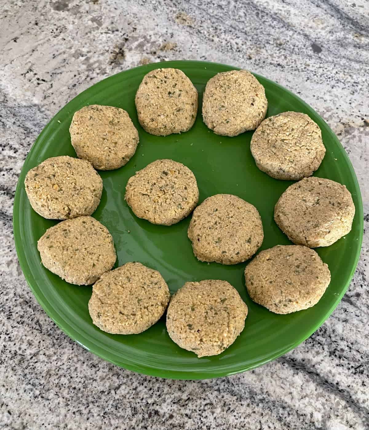 Uncooked falafel patties on large green plate on granite.