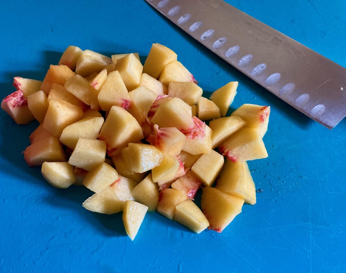 Diced peaches on blue cutting board with knife alongside.