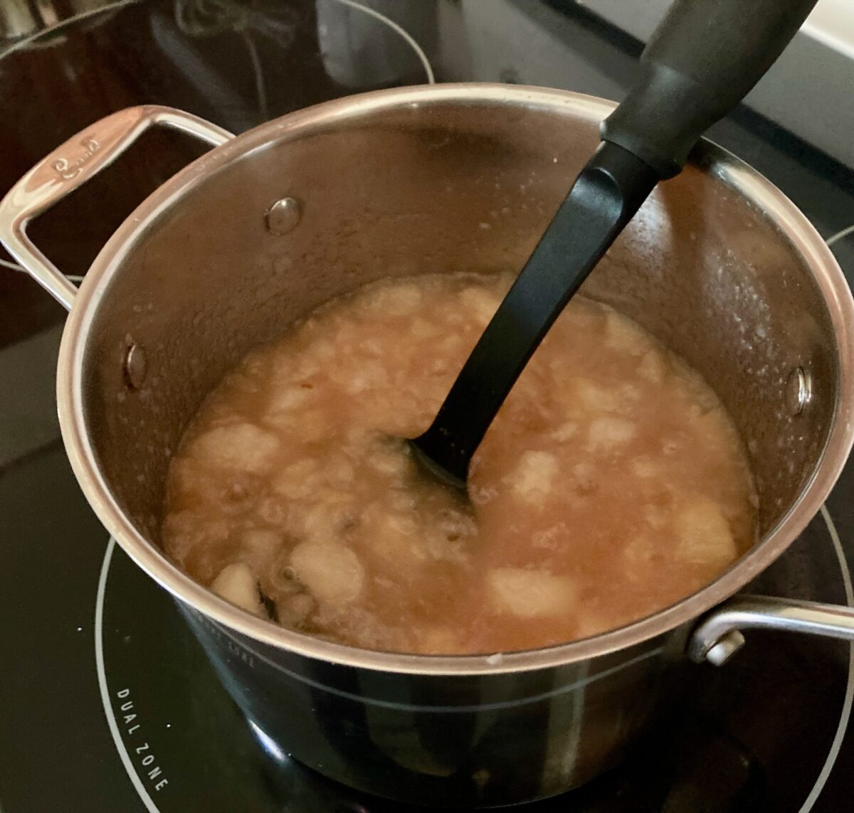Mashing apple, pear compote in pot.