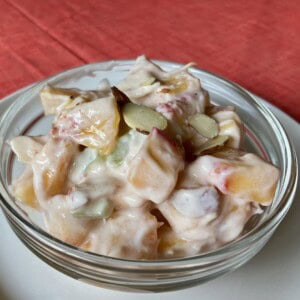 peach salad in a clear glass bowl set on a white plate under an orange tablecloth