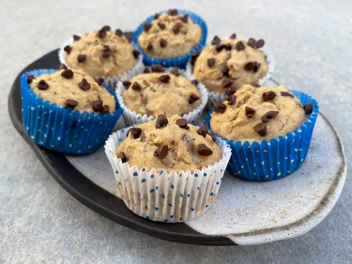 Fresh baked banana chocolate chip pancake muffins in blue and white paper liners on ceramic serving platter.