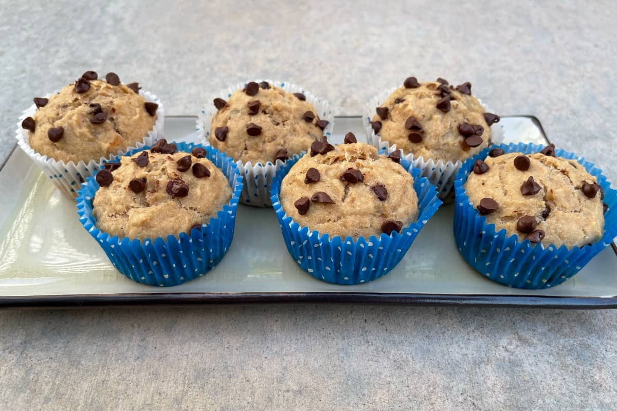 Fresh baked banana chocolate chip pancake muffins in blue and white paper liners and rectangular serving platter.