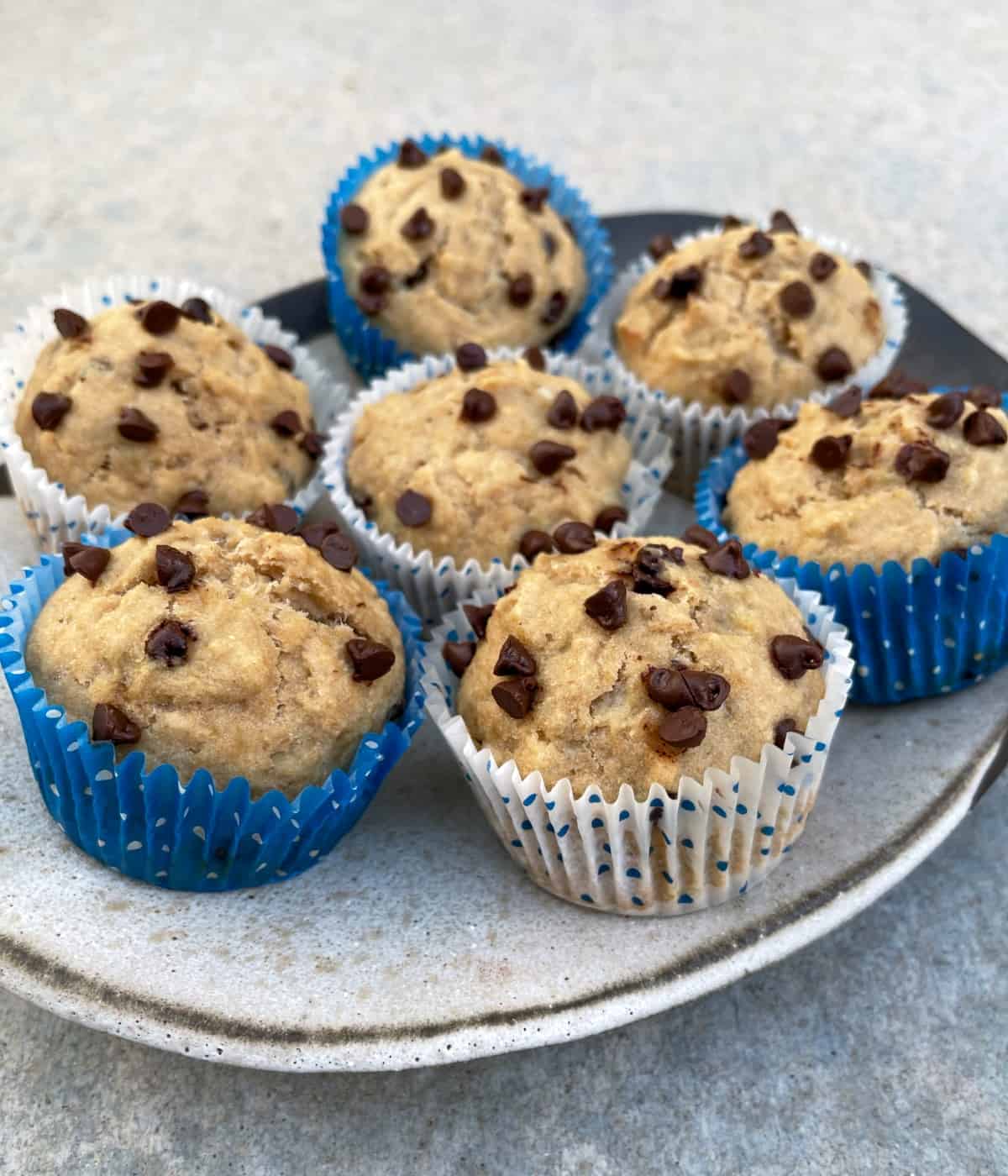 Banana chocolate chip muffins in blue and white paper liners on ceramic plate.