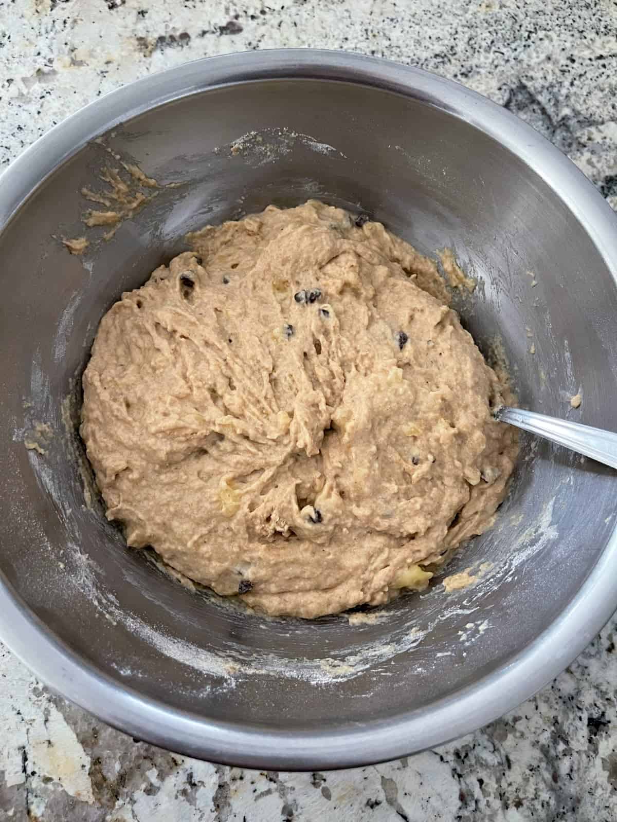 Mixing banana chocolate chip pancake batter in stainless mixing bowl with spoon.