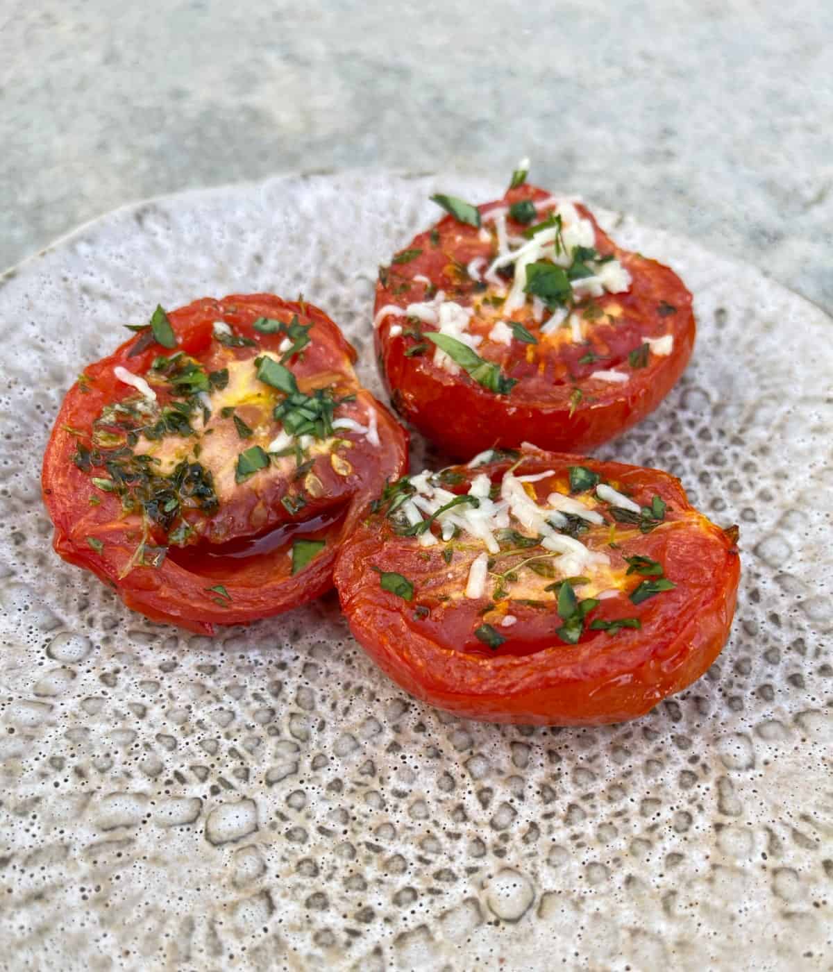 Three parmesan broiled tomato halves on small ceramic plate.