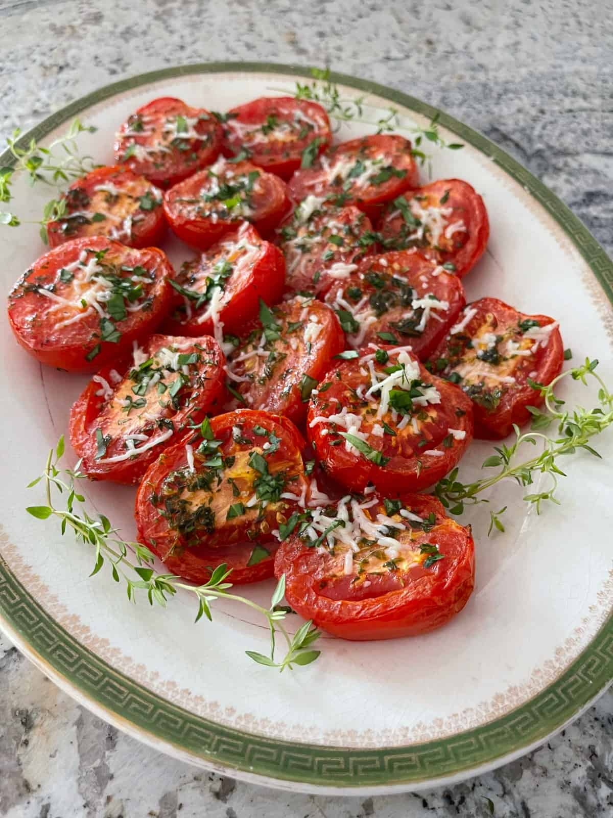 Parmesan broiled tomatoes topped with fresh chopped basil on vintage serving platter garnished with fresh thyme.