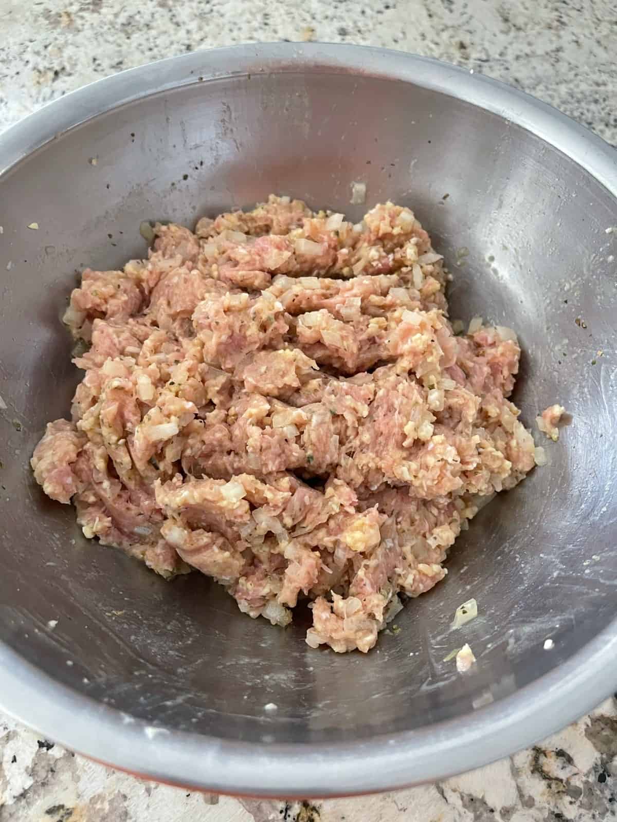 Combining ingredients in mixing bowl for making turkey meatballs.