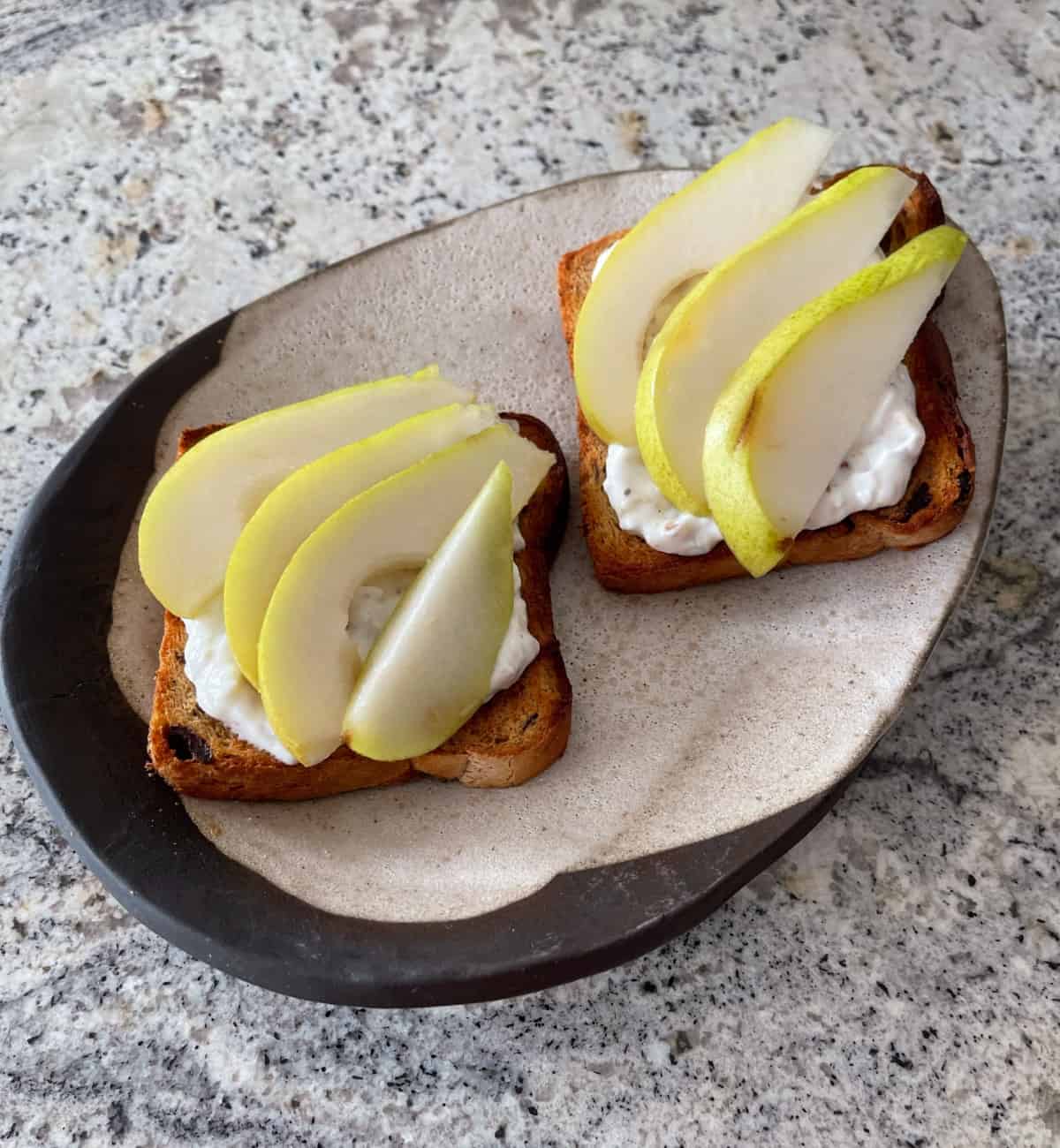 Cinnamon swirl raisin toast topped with honey-walnut yogurt spread and fresh sliced pears on ceramic plate.