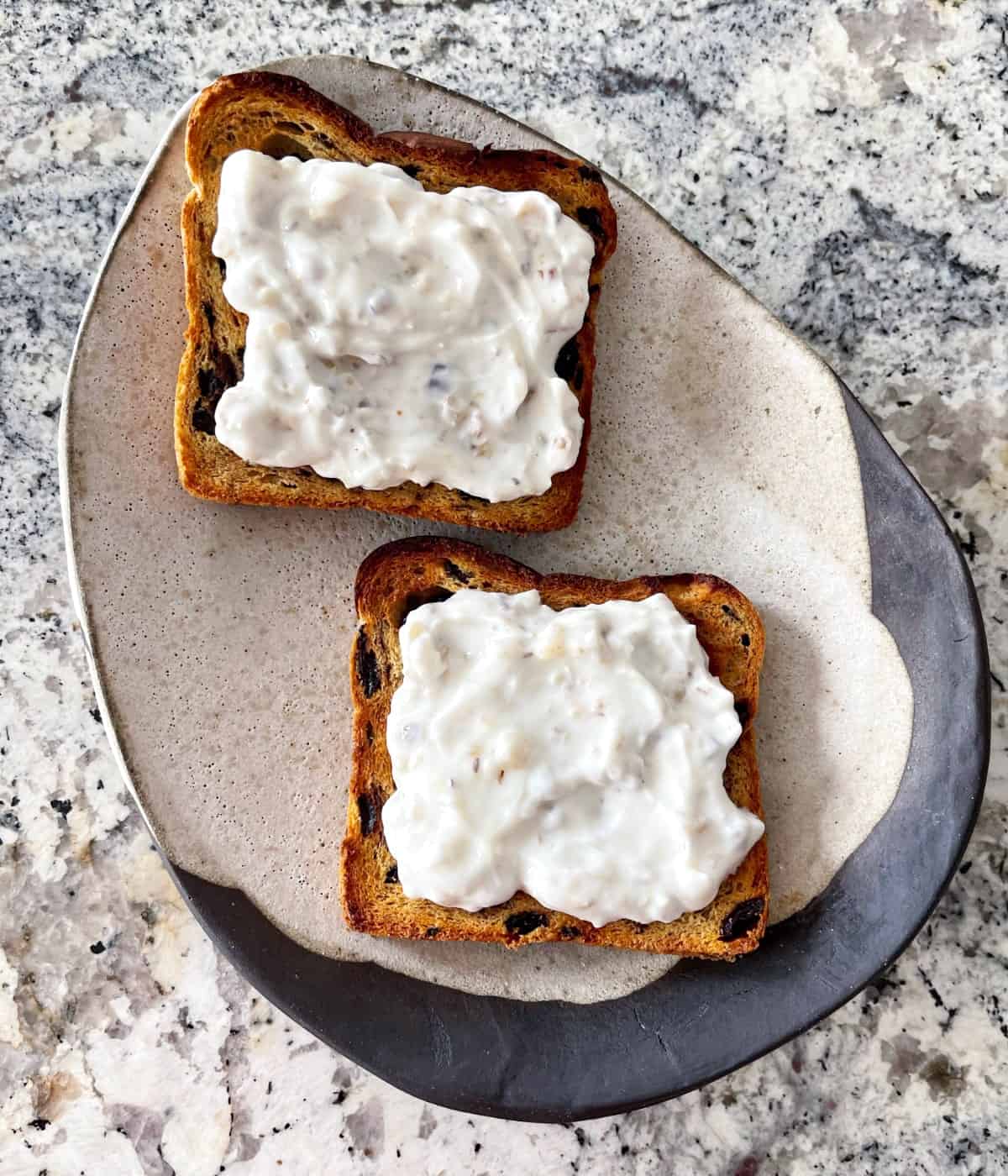 Cinnamon raisin toast topped with honey-walnut yogurt spread on ceramic plate.