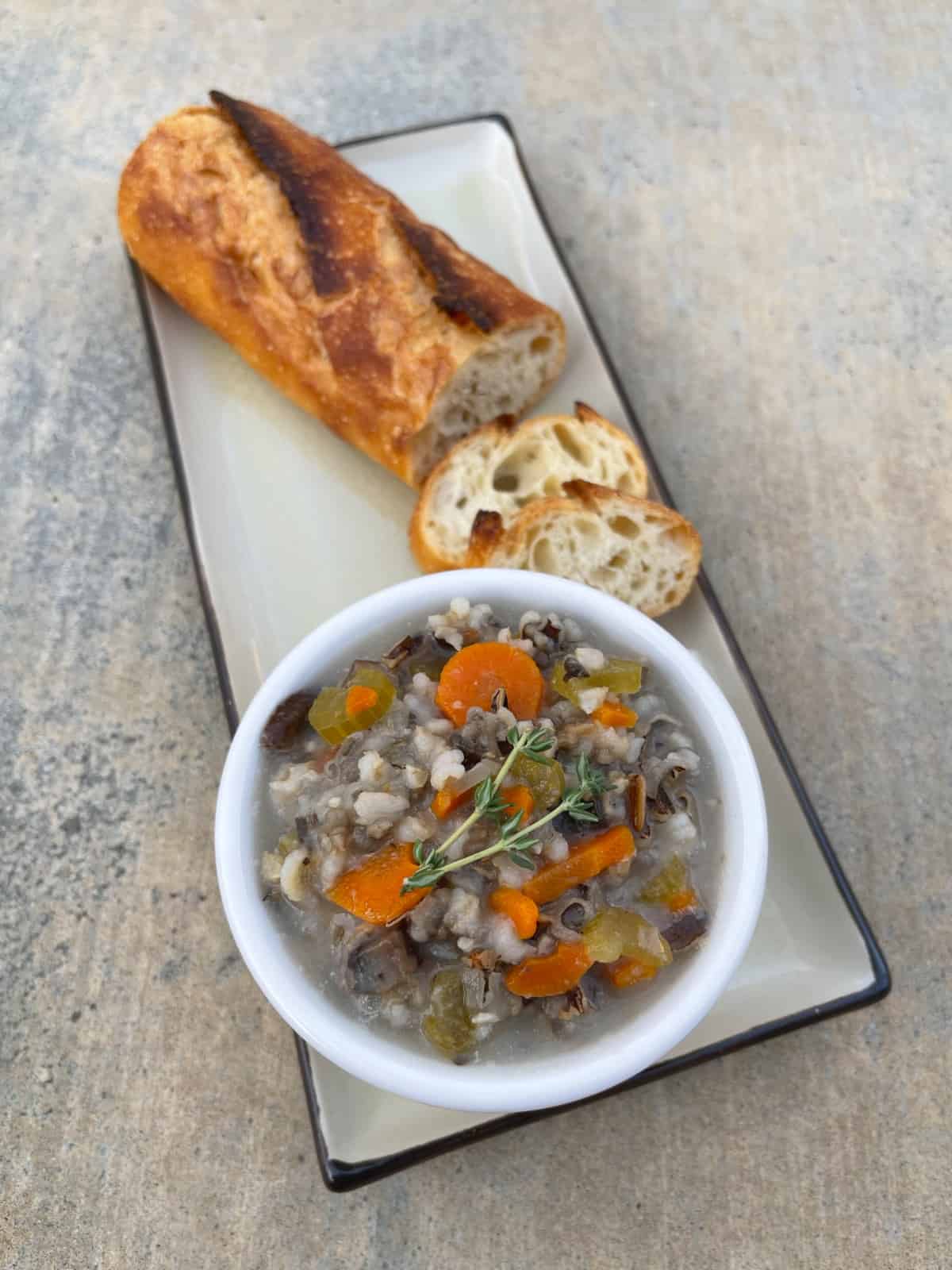 Wild Rice and Mushroom Vegetable Stew in small white bowl on plate with fresh sliced sourdough baguette.
