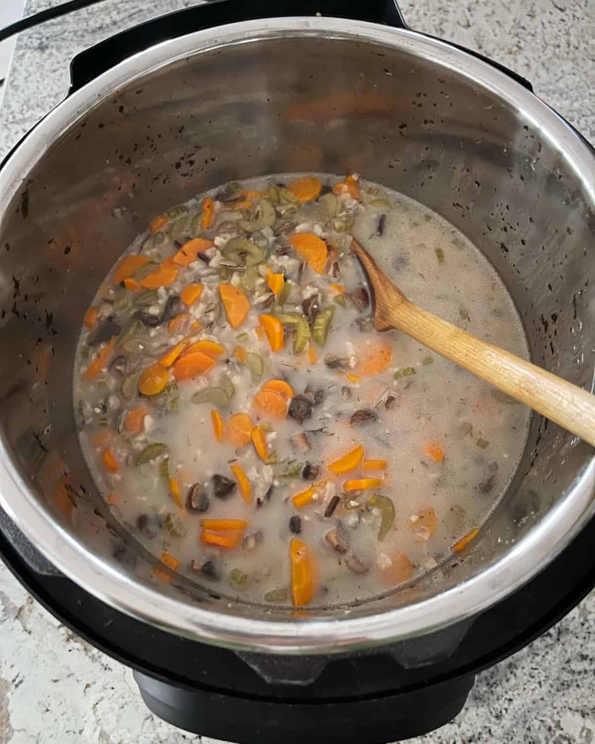 Stirring coconut milk into Instant Pot Wild Rice and Vegetable Stew with wooden spoon.