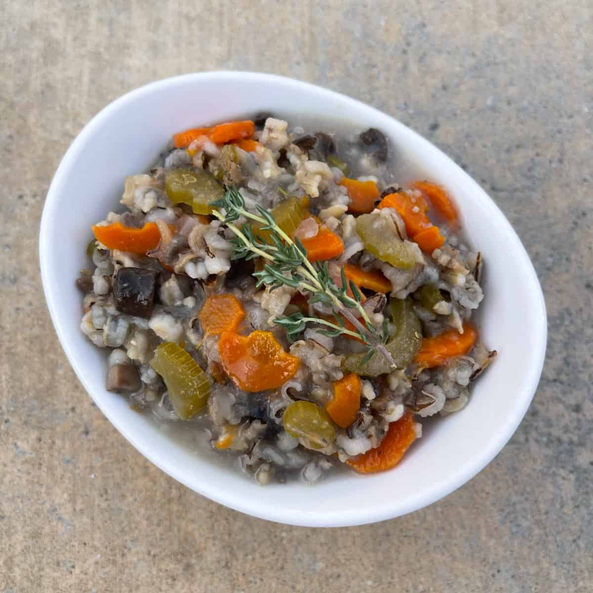 Instant Pot Wild Rice and Mushroom Vegetable Stew garnished with fresh thyme in small white bowl.