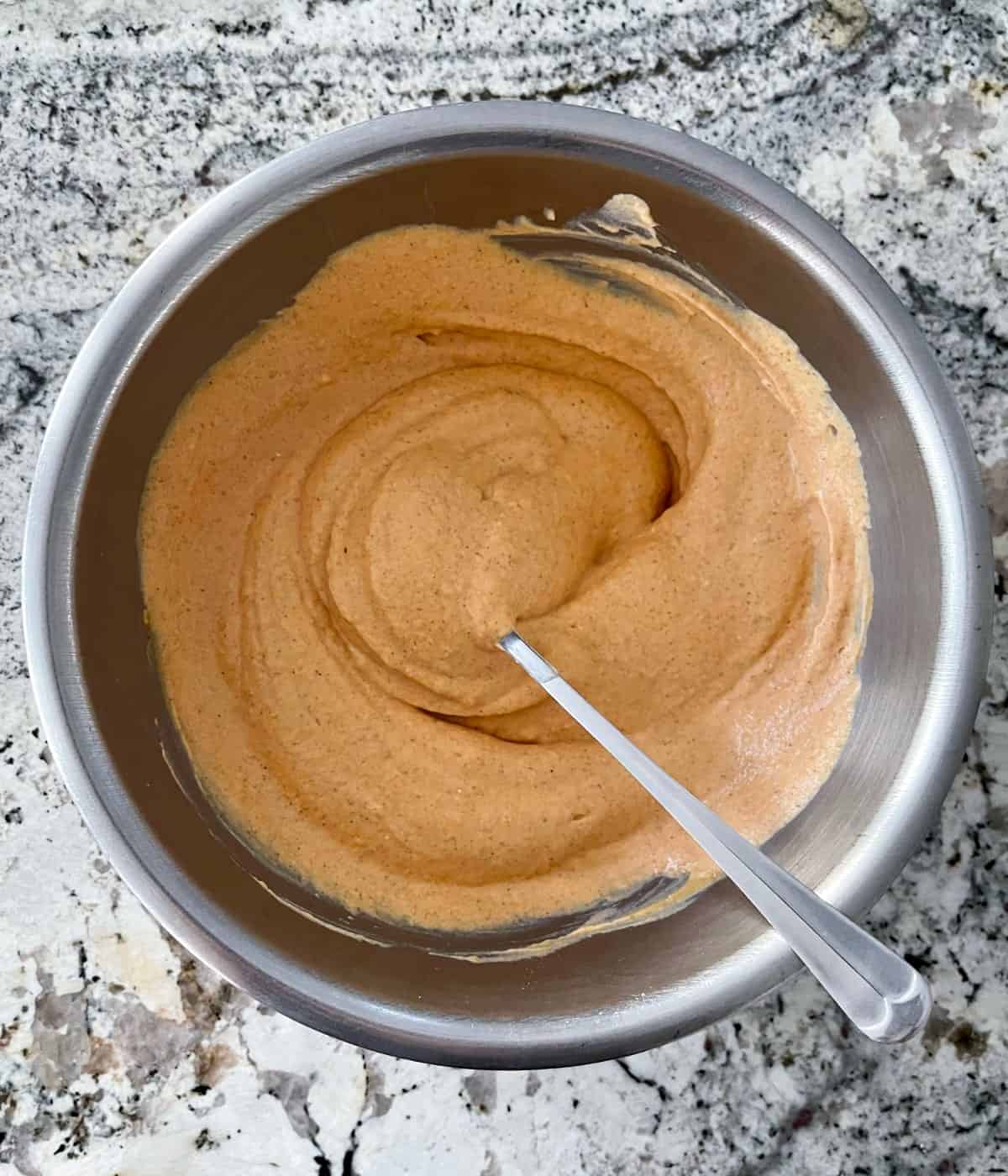 Stirring mixture for pumpkin yogurt parfaits in mixing bowl with spoon.