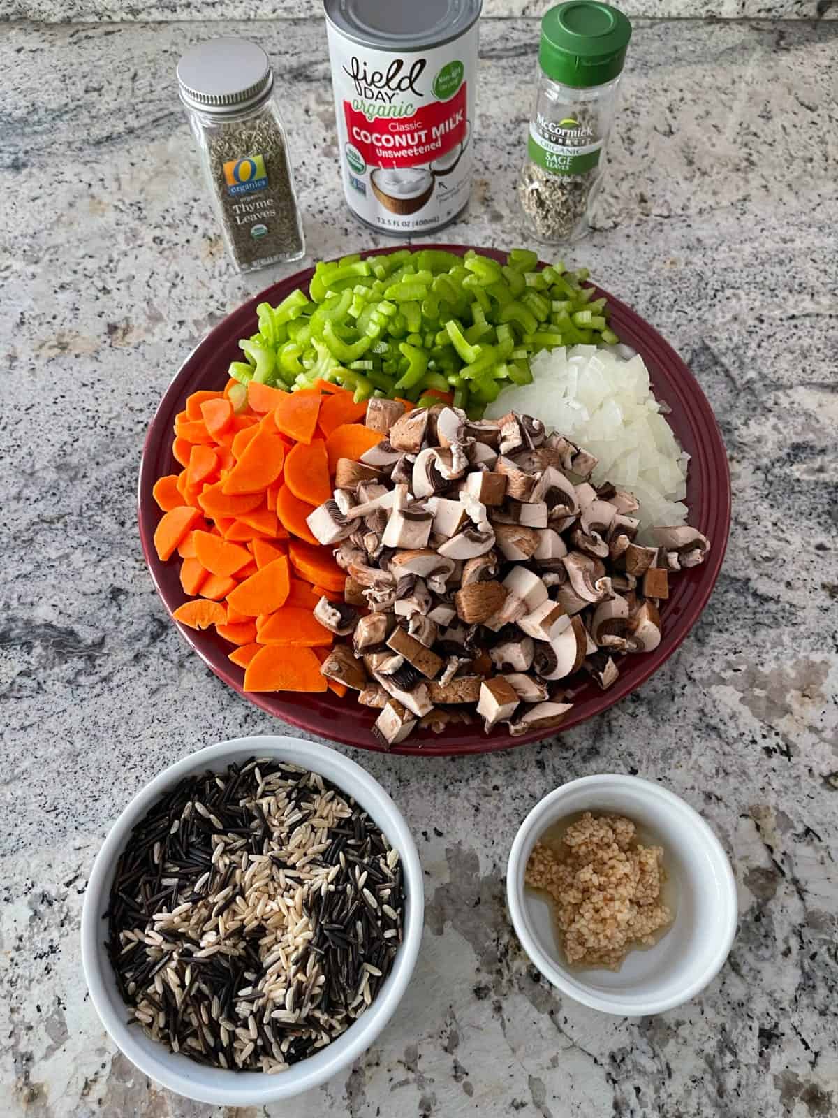 Ingredients including wild rice and brown rice blend, minced garlic, chopped mushrooms, celery, carrots and onion, dried thyme and sage with can of coconut milk.
