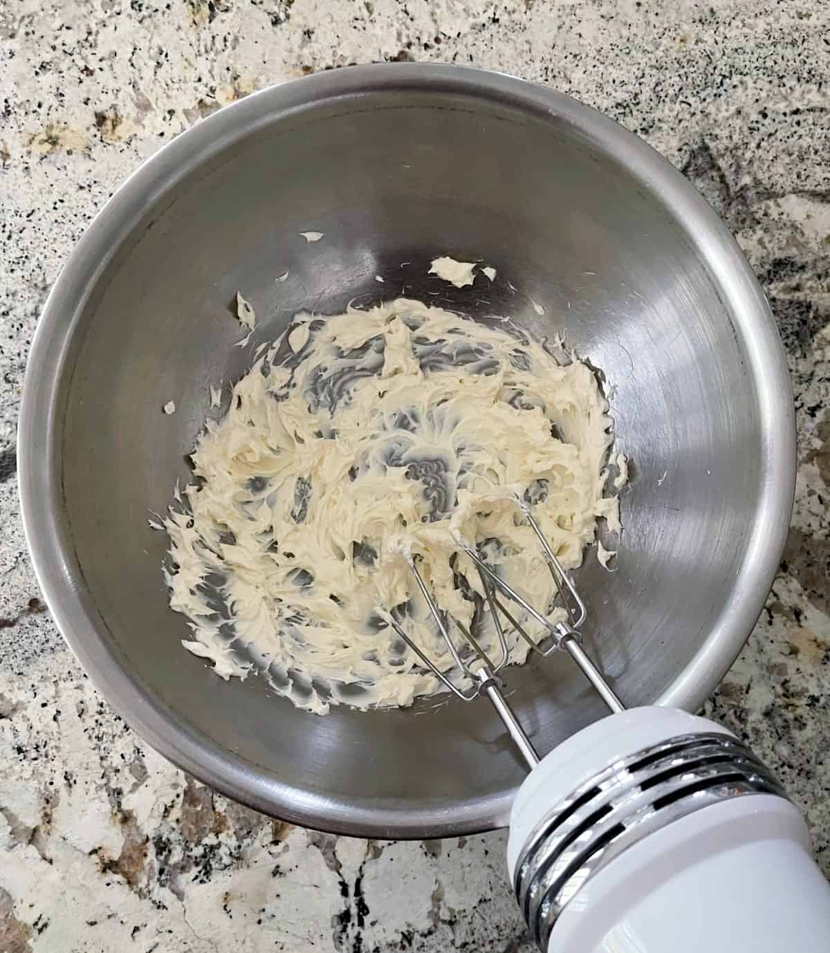 Beating light cream cheese in mixing bowl with electric hand mixer.