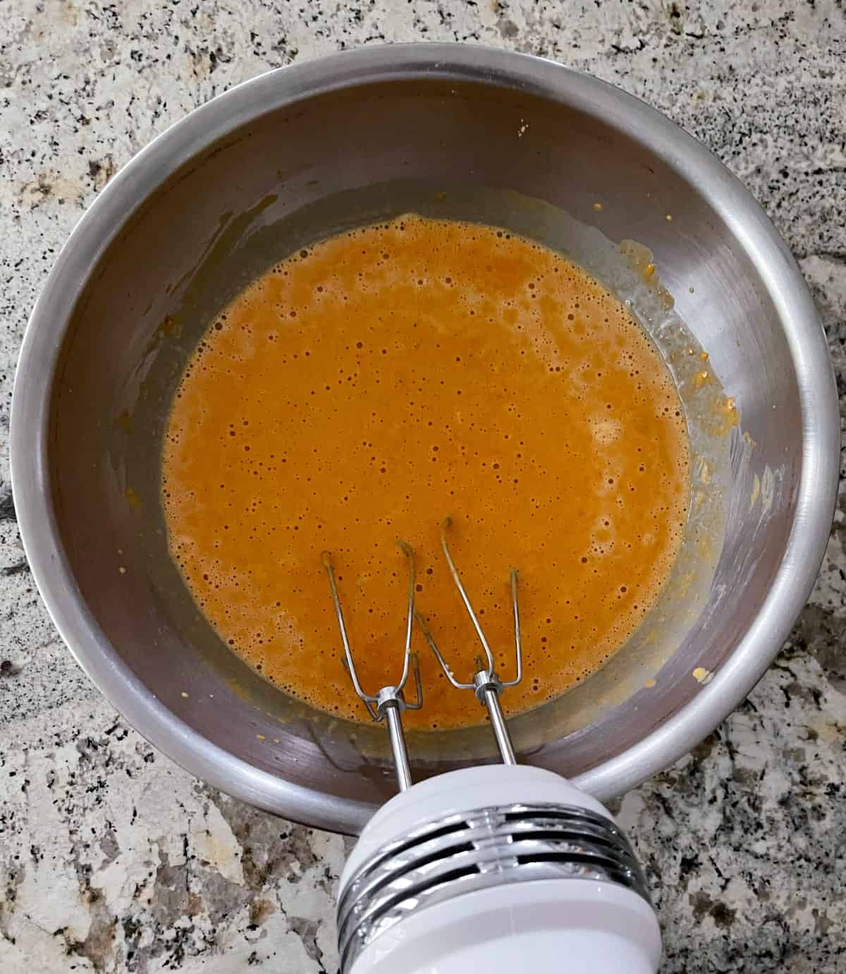 Beating pumpkin pie custard in stainless bowl with hand mixer.