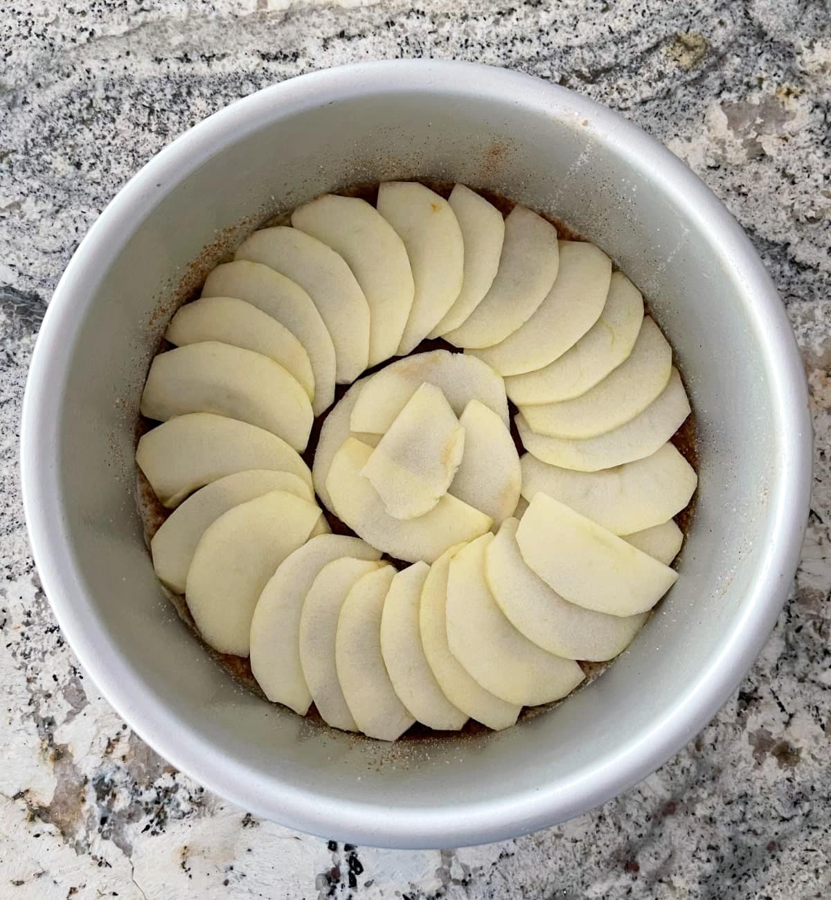 Round cake pan layered with melted butter, cinnamon-sugar mixture and thinly sliced apples.