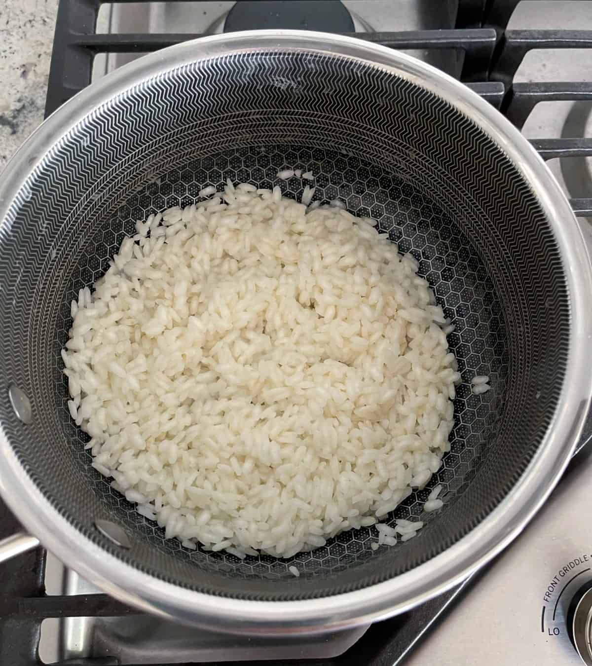 Cooked arborio rice in saucepan on stove top.
