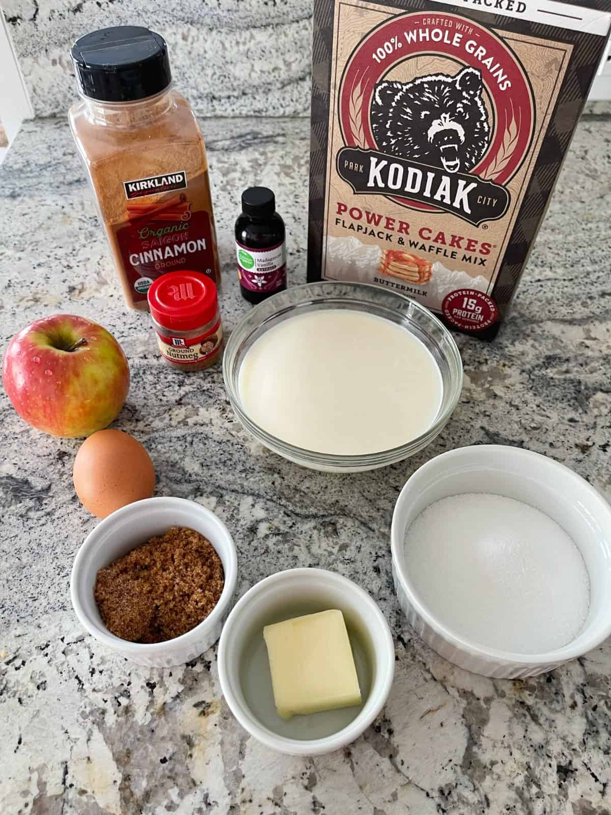Ingredients including Kodiak Power Cakes flapjack and waffle mix, cinnamon, nutmeg, vanilla extract, apple, egg, butter, Truvia sweetener and butter on granite.