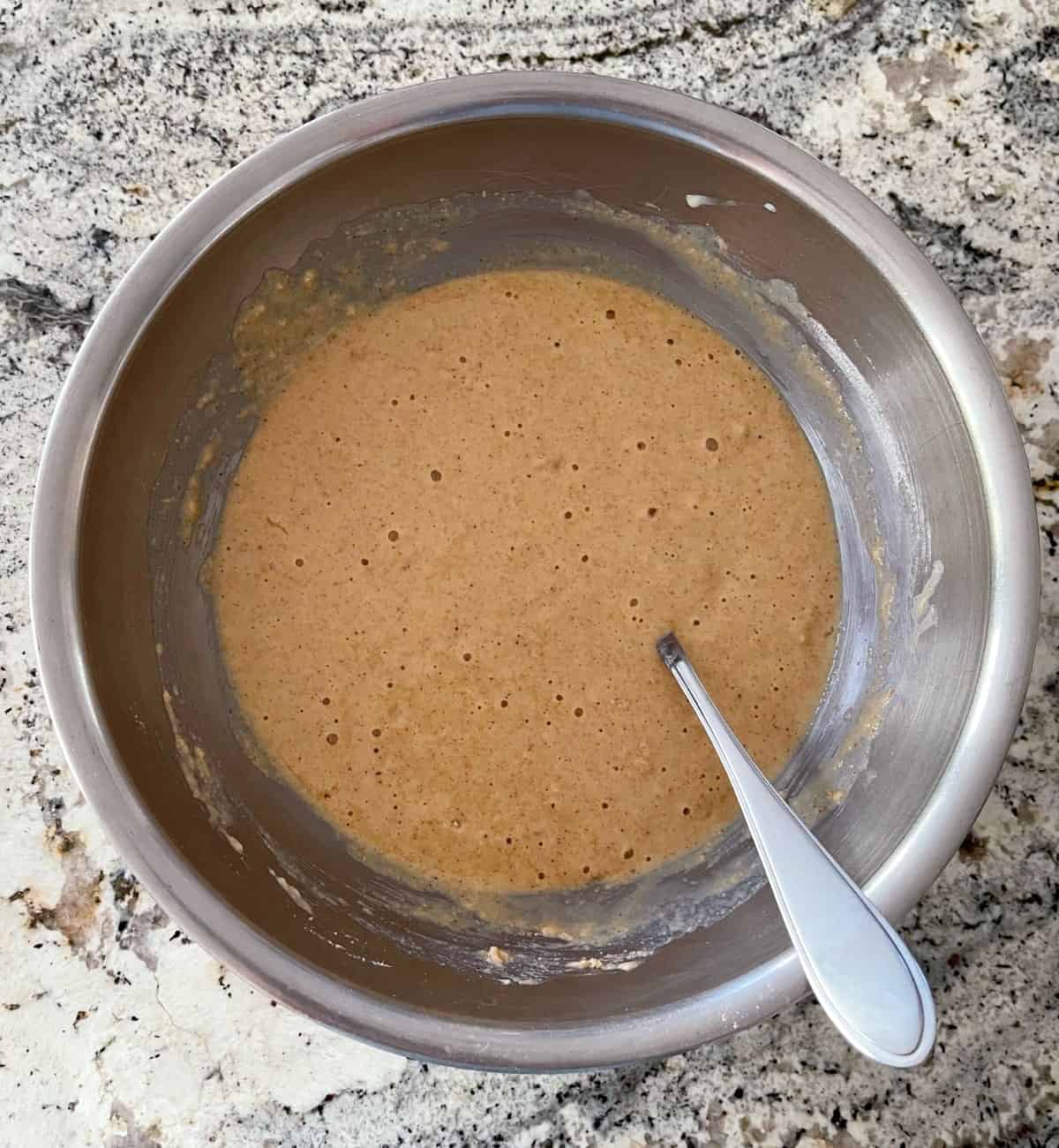 Stirring cinnamon apple quick cake batter in mixing bowl with large spoon.