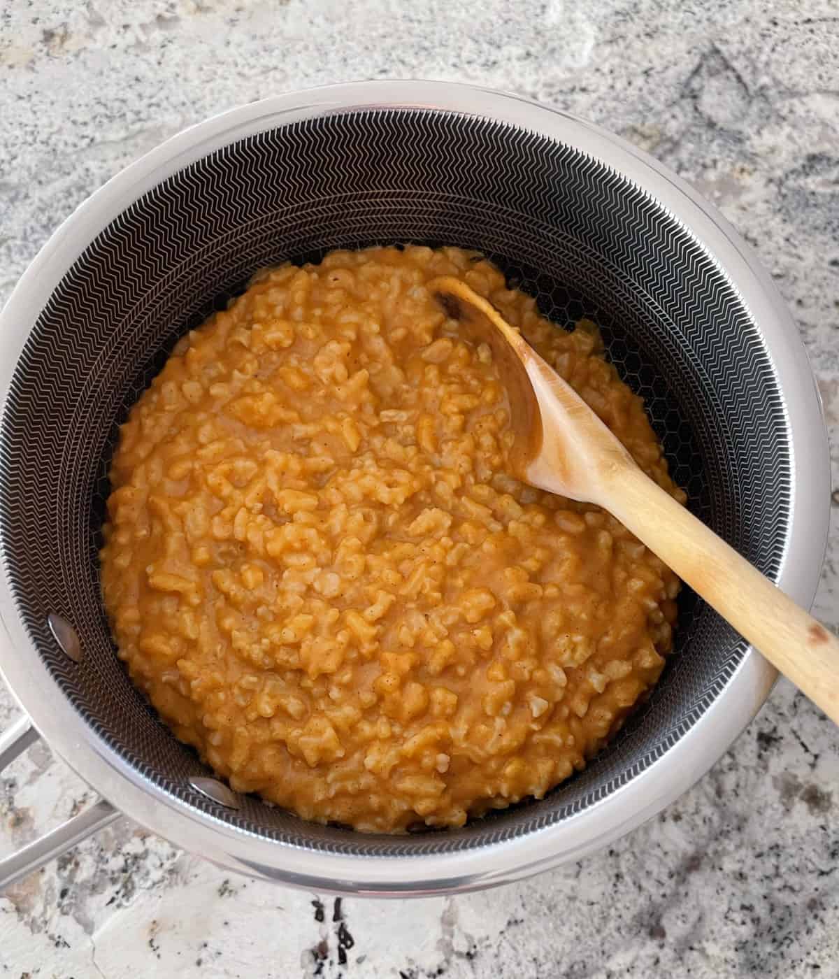 Pumpkin rice pudding in saucepan with wooden spoon.