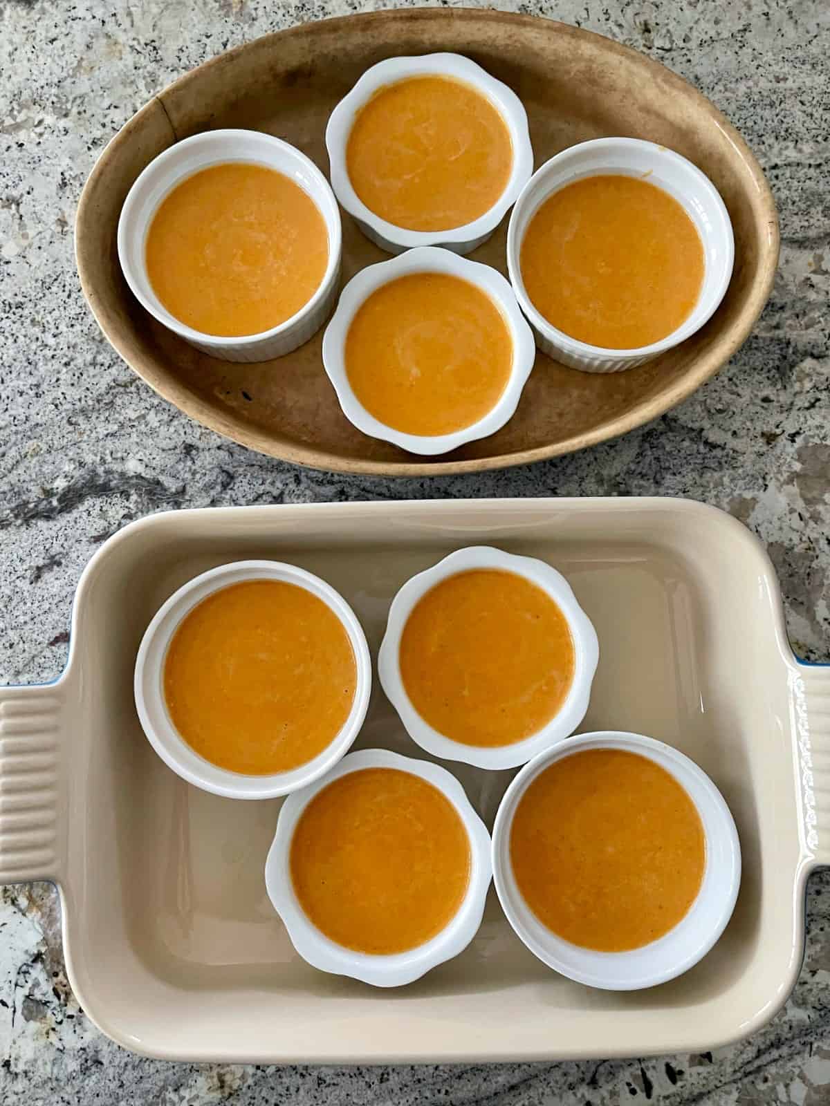 Eight ramekins with unbaked pumpkin pie custard in two large baking dishes.