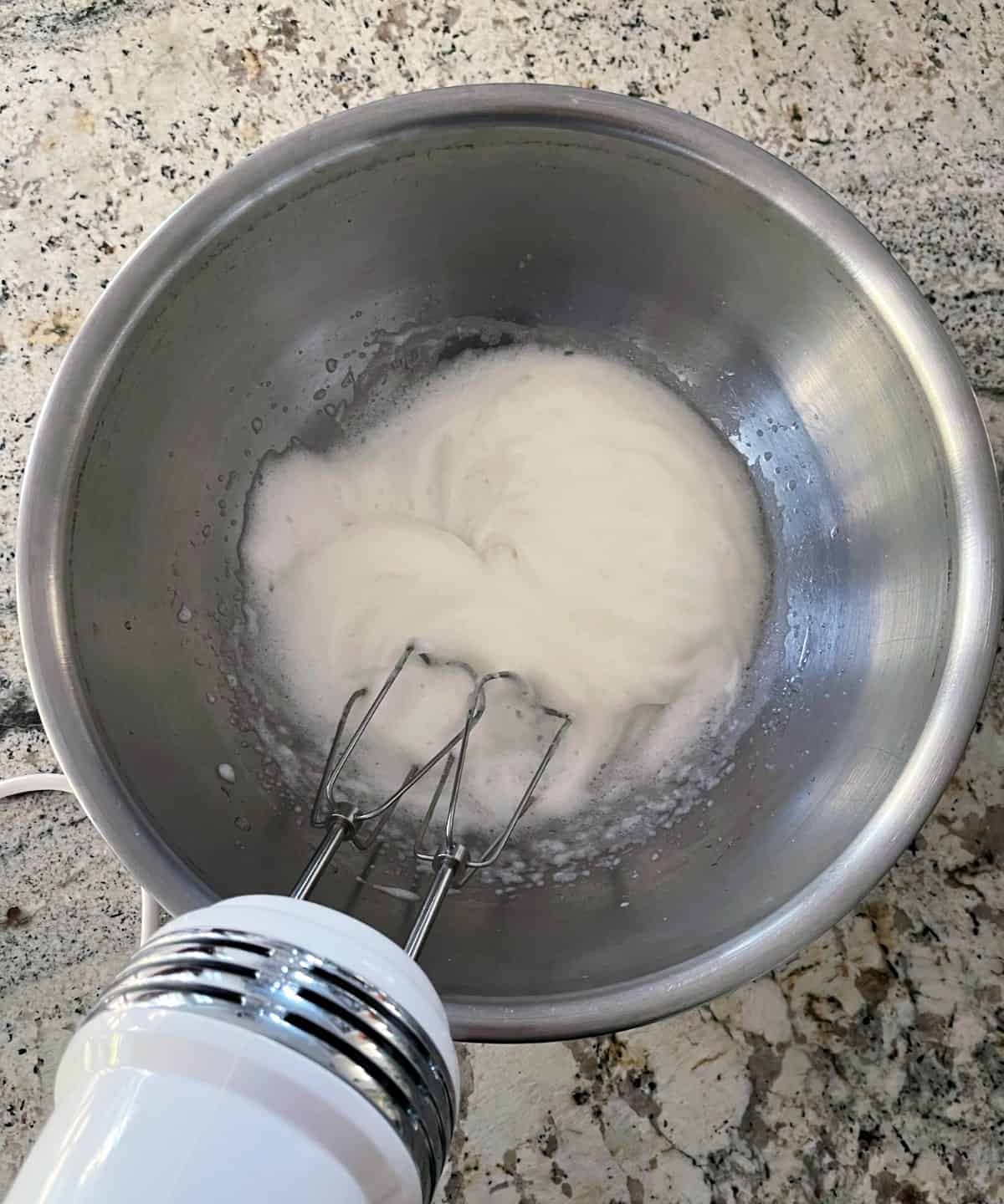 Beating egg whites in mixing bowl with handheld electric mixer.