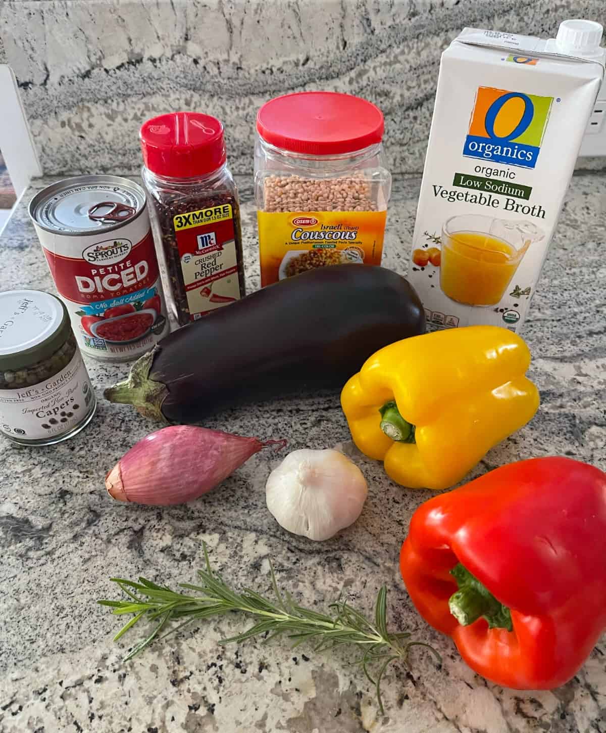 Ingredients including capers, canned diced tomatoes, crushed red pepper flakes, Israeli couscous, vegetable broth, eggplant, red and yellow bell peppers, garlic, shallot and sprig of rosemary.