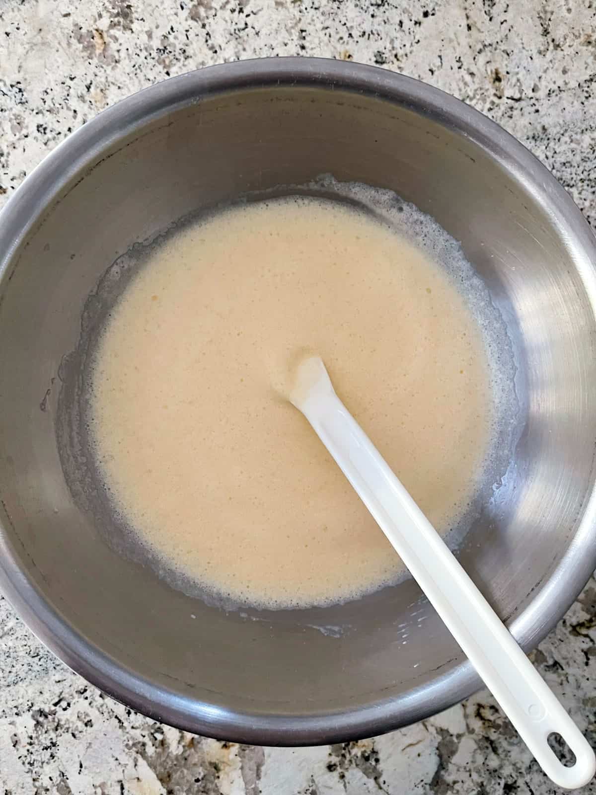 Folding egg whites into egg whites with white spatula in stainless mixing bowl.