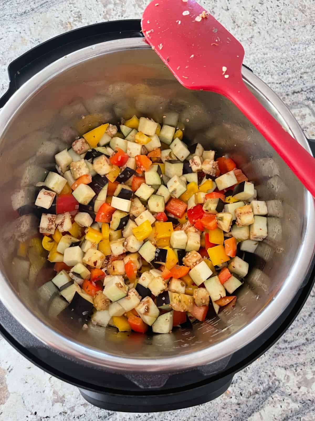 Sautéing diced eggplant with red and yellow bell peppers in Instantpot with red silicone spatula.