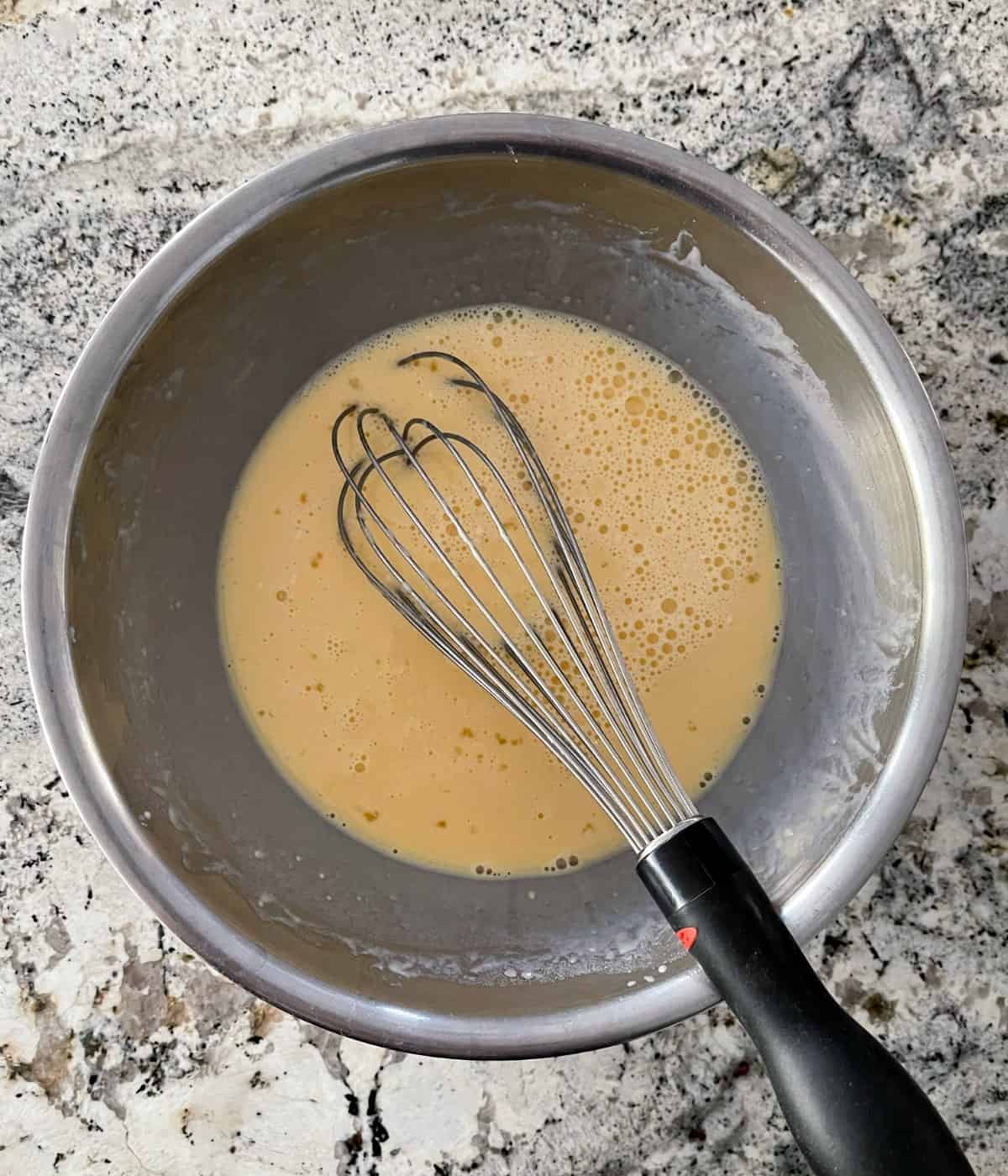 Whisking egg yolks, milk, flour and salt in stainless mixing bowl.