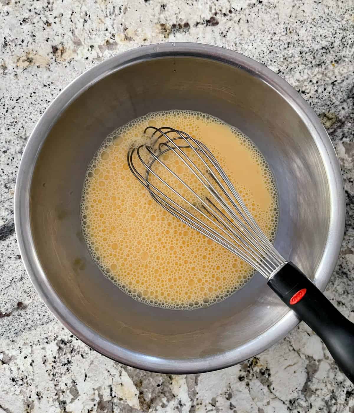 Whisking egg yolks and milk in stainless mixing bowl.