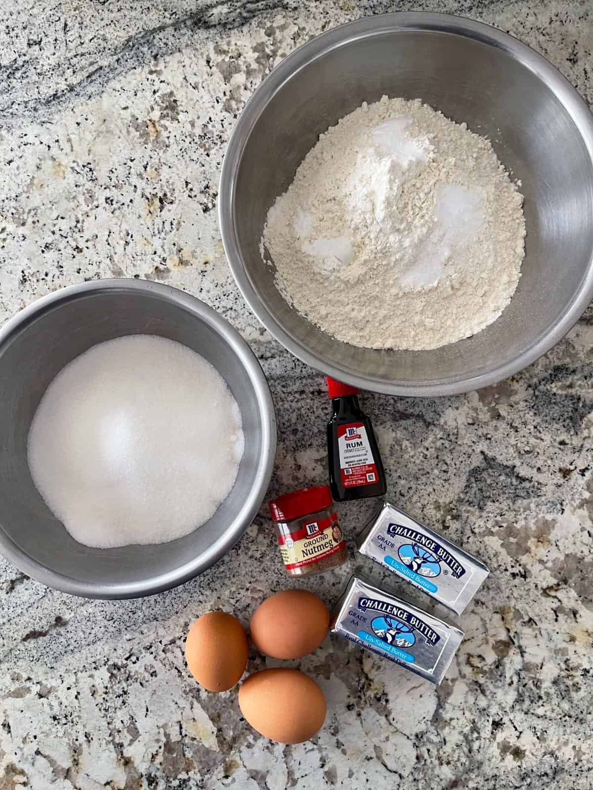 Cookie ingredients including mixing bowl with all-purpose flour, cream of tartar and baking soda, bowl of sugar, unsalted butter, 3 eggs, rum extract and ground nutmeg.