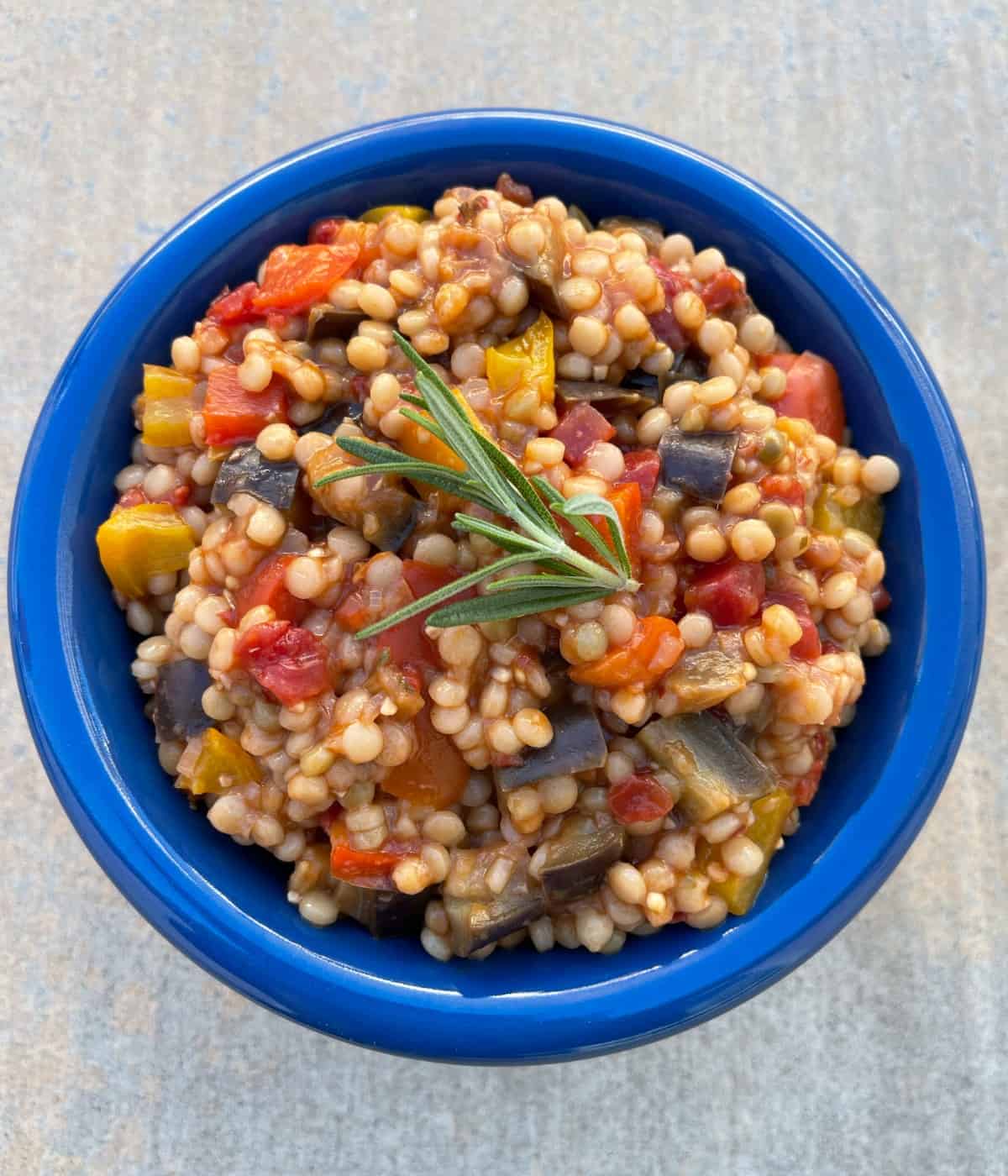 Instant pot Israeli couscous puttanesca in blue serving bowl with sprig of fresh rosemary.