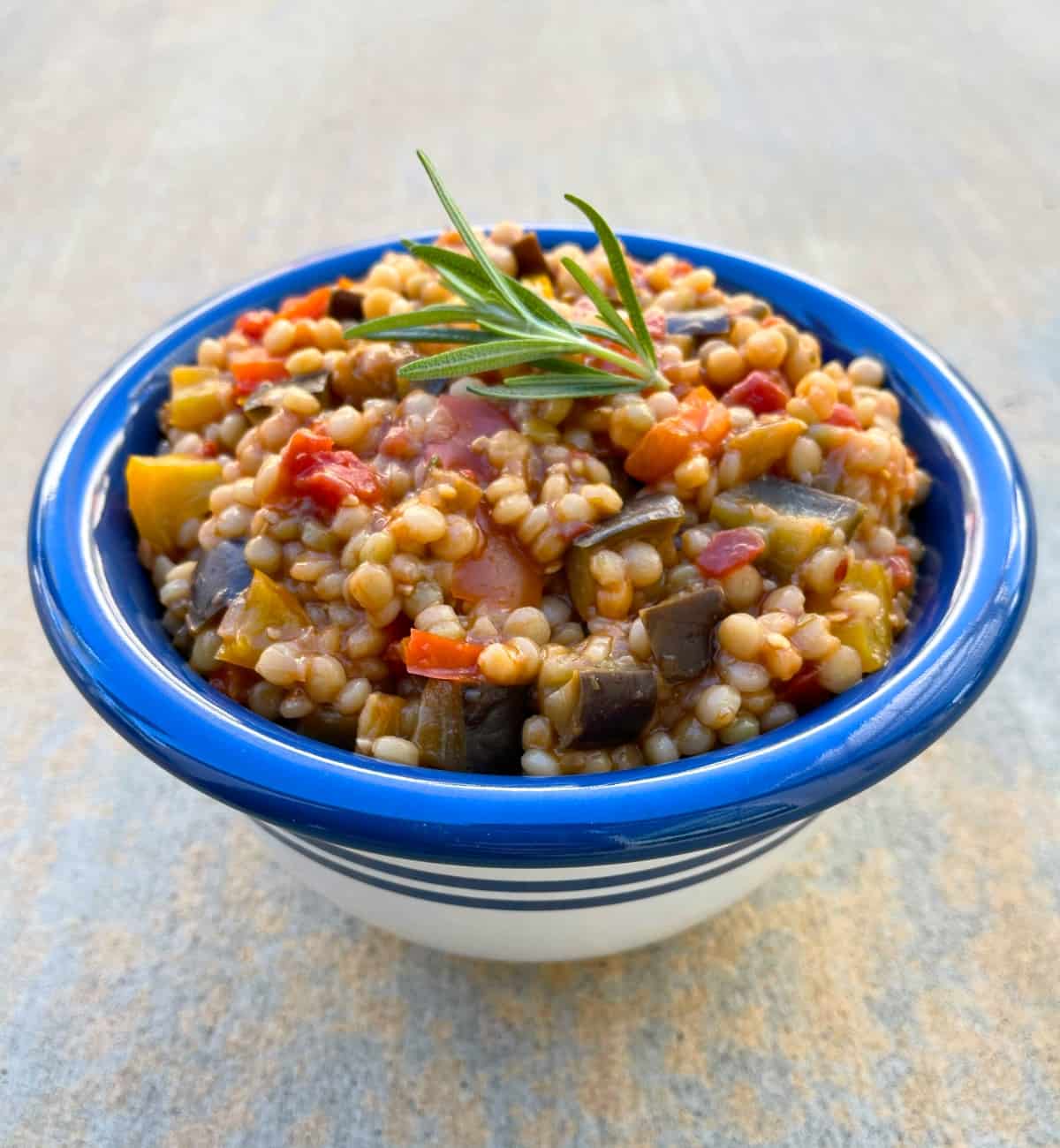 Pearl couscous with peppers and eggplant in blue and white serving bowl.
