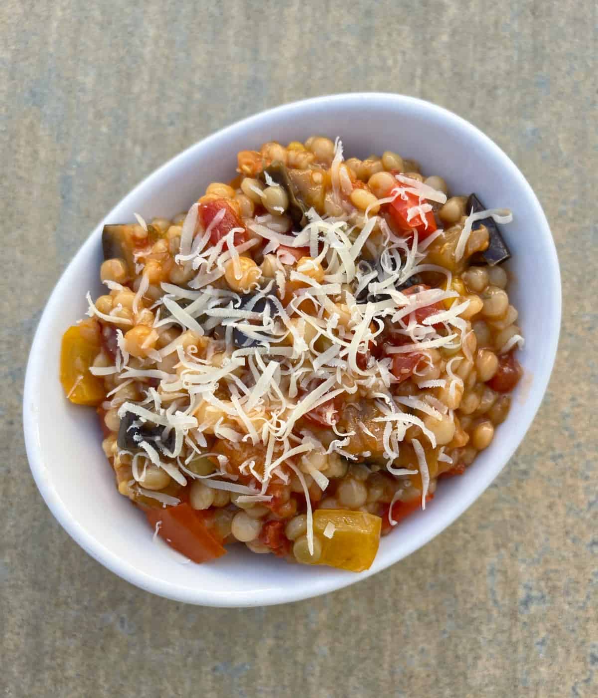 Instantpot Israeli couscous with eggplant and peppers topped with grated Parmesan cheese in white bowl.
