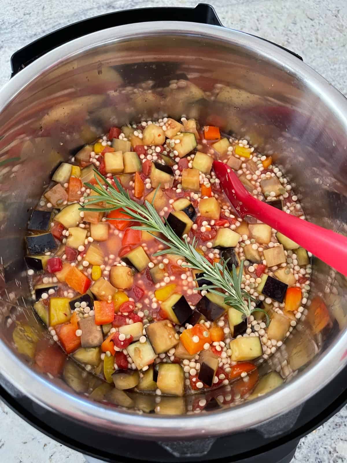 Uncooked couscous puttanesca with fresh rosemary sprig in Instantpot.