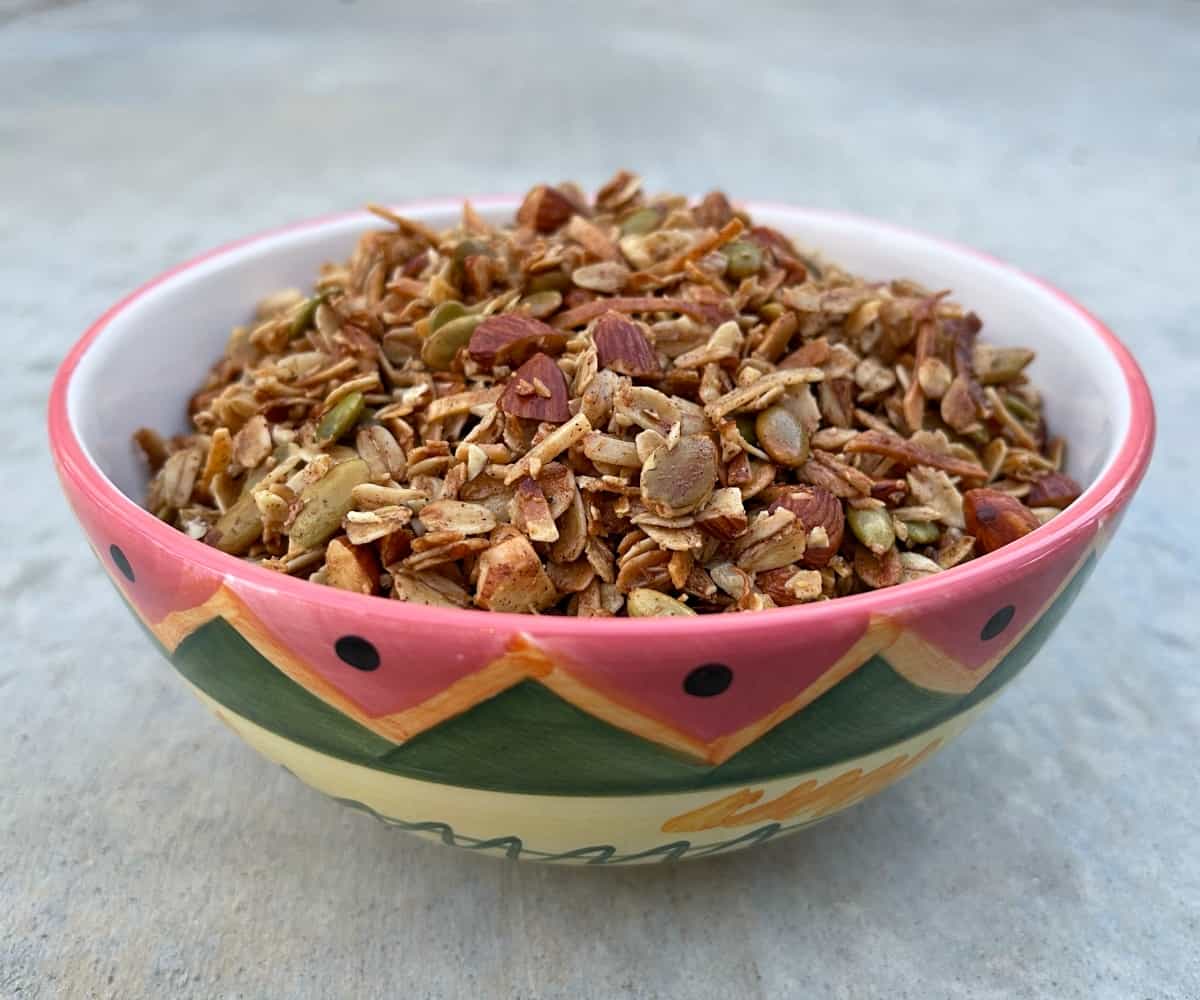 Fresh cooked air fryer toasted oat granola with pumpkin seeds and chopped almonds in colorful hand-painted bowl.